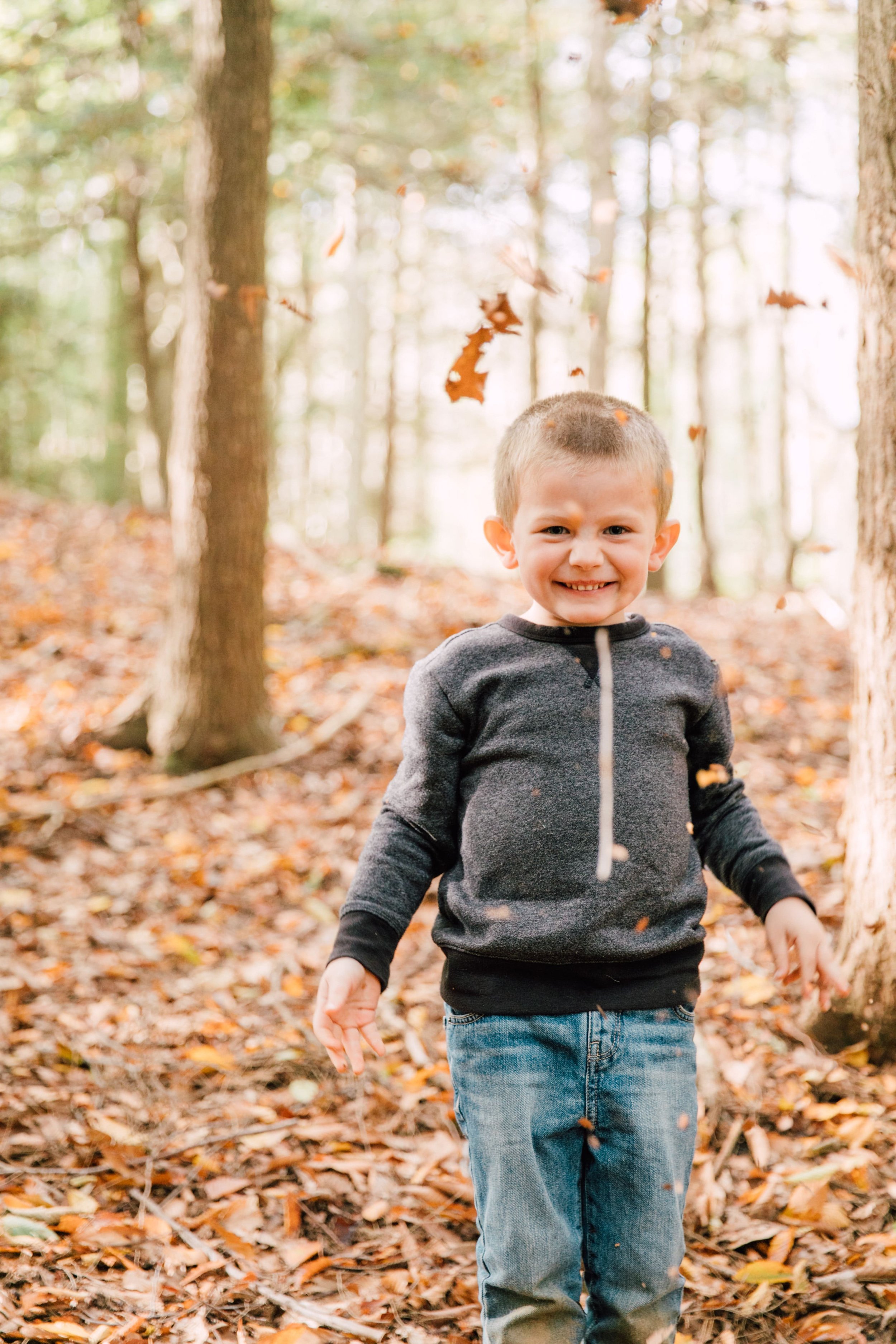  a boy stands smiling with leaves falling during a backyard photoshoot 