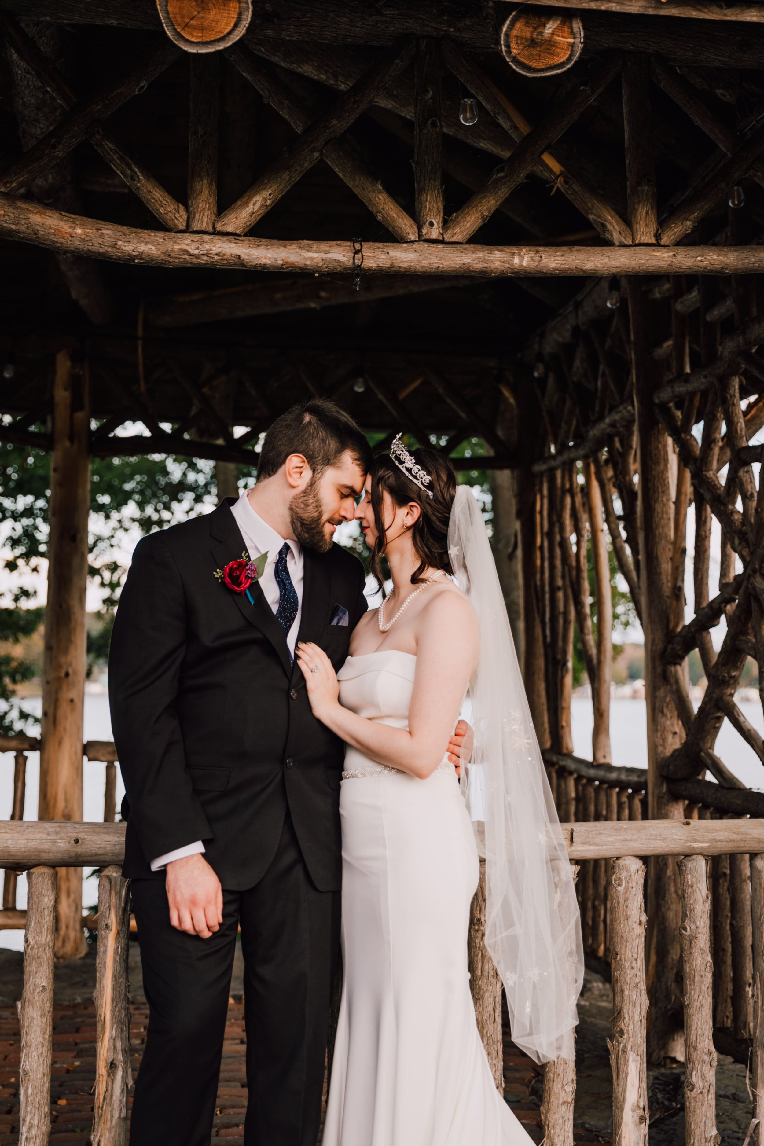  the bride and groom stand in front of a gazebo with their foreheads pressed together at their lake ontario wedding 
