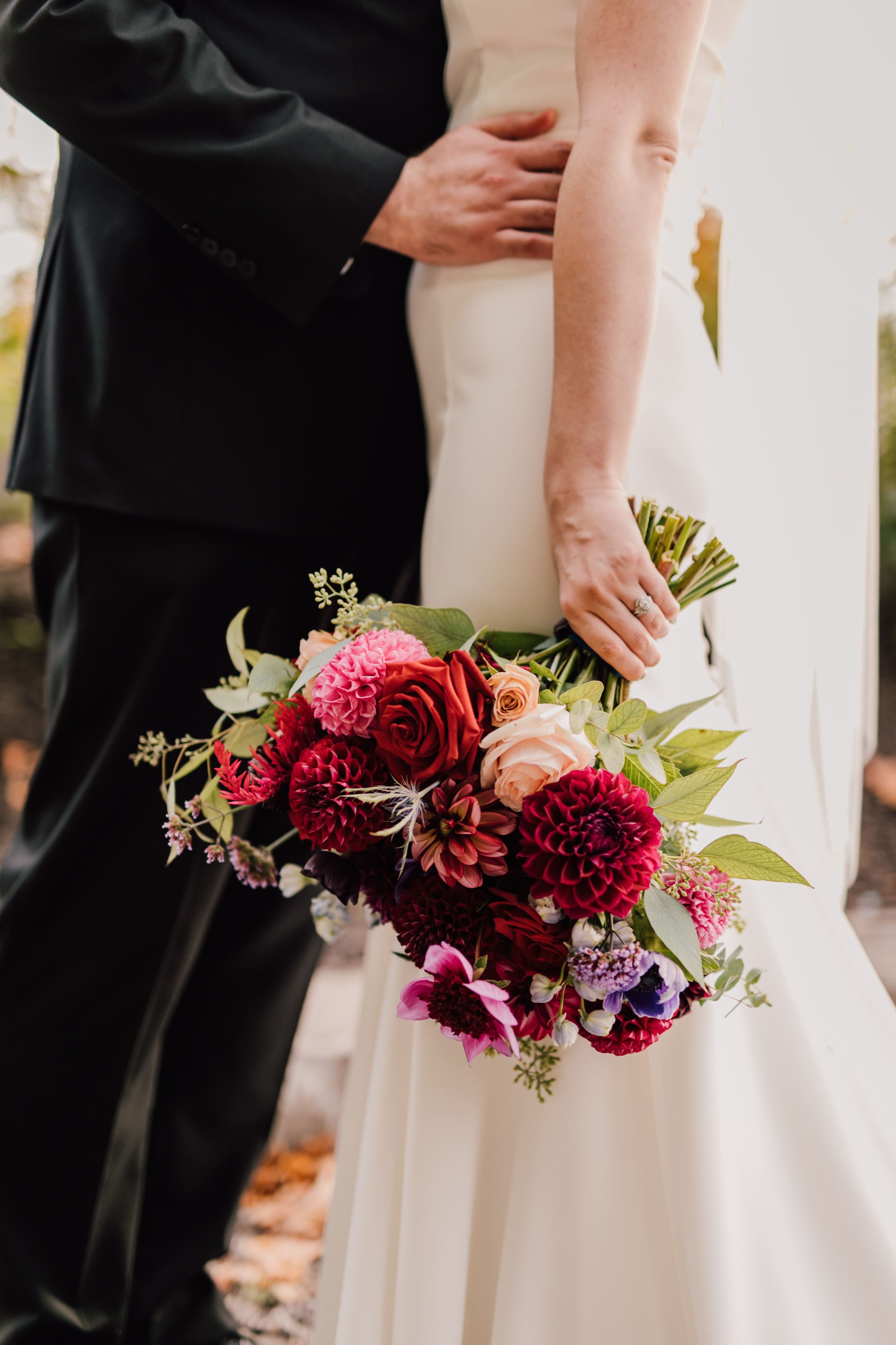  the bride holds her red, pink, and purple bouquet as she stands close to her husband during their october space wedding 