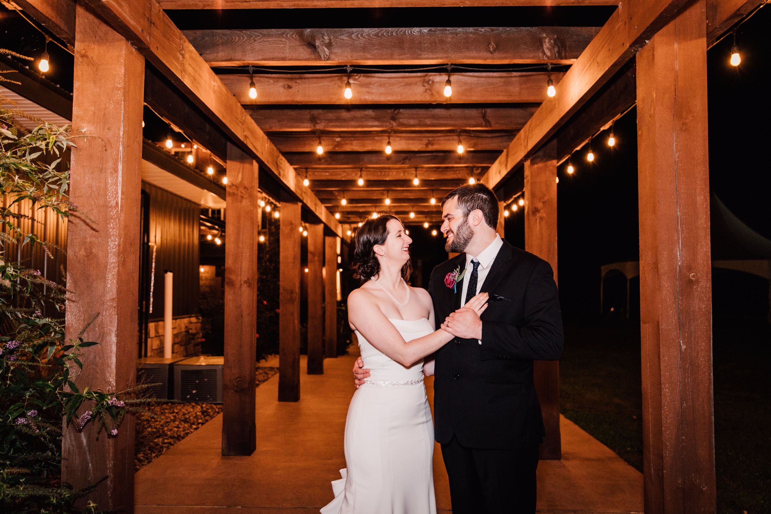  the bride and groom smile at each other as they stand under string lights at their starry night wedding 