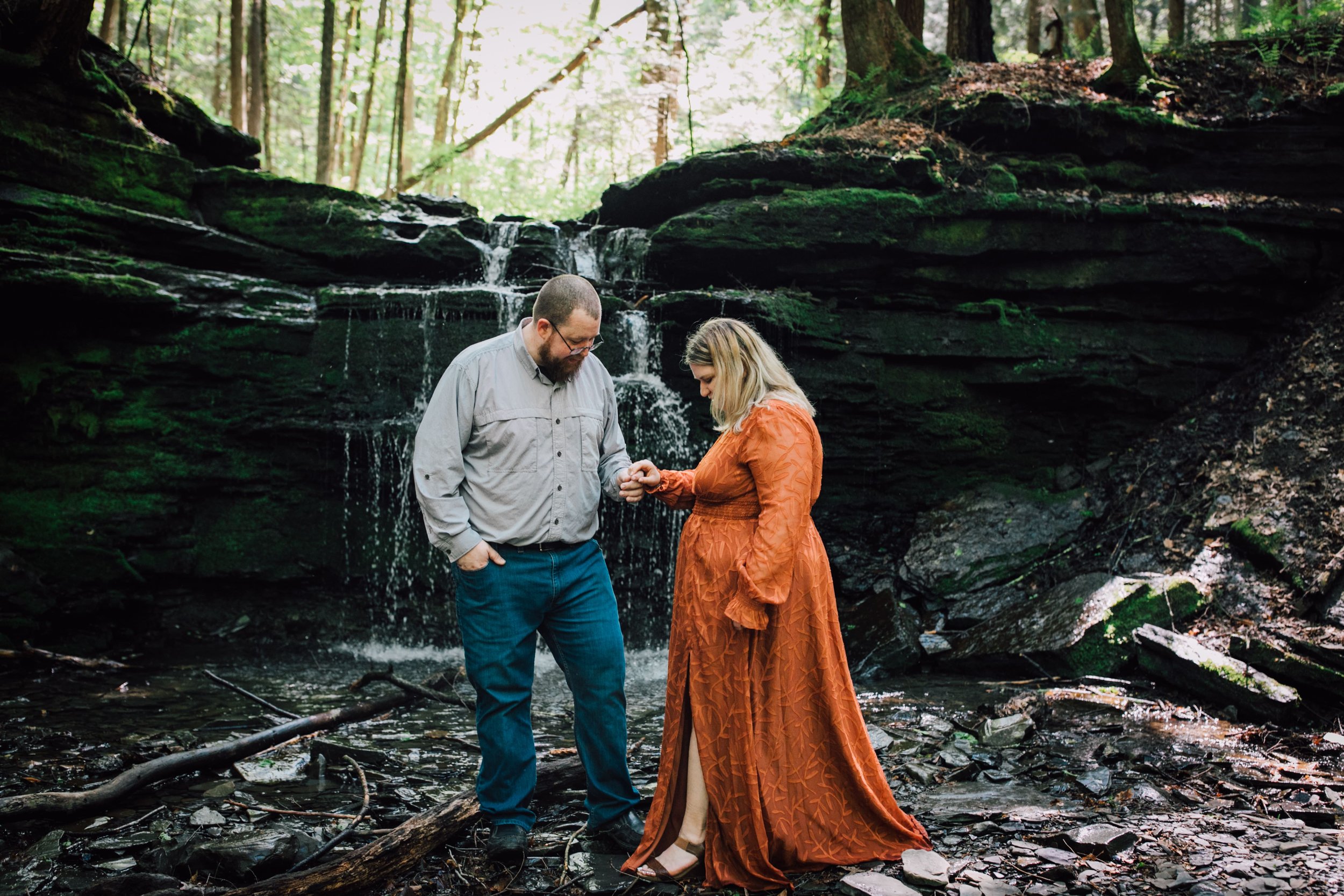  patrick helps brittany step across the stream in front of a beautiful waterfall engagement photos session 