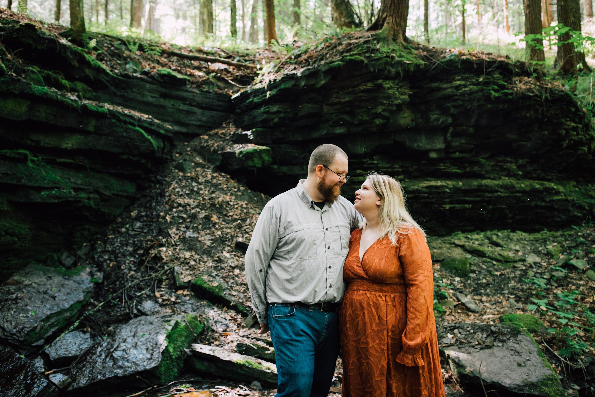  engaged couple look at each other as they post for forest engagement photos 