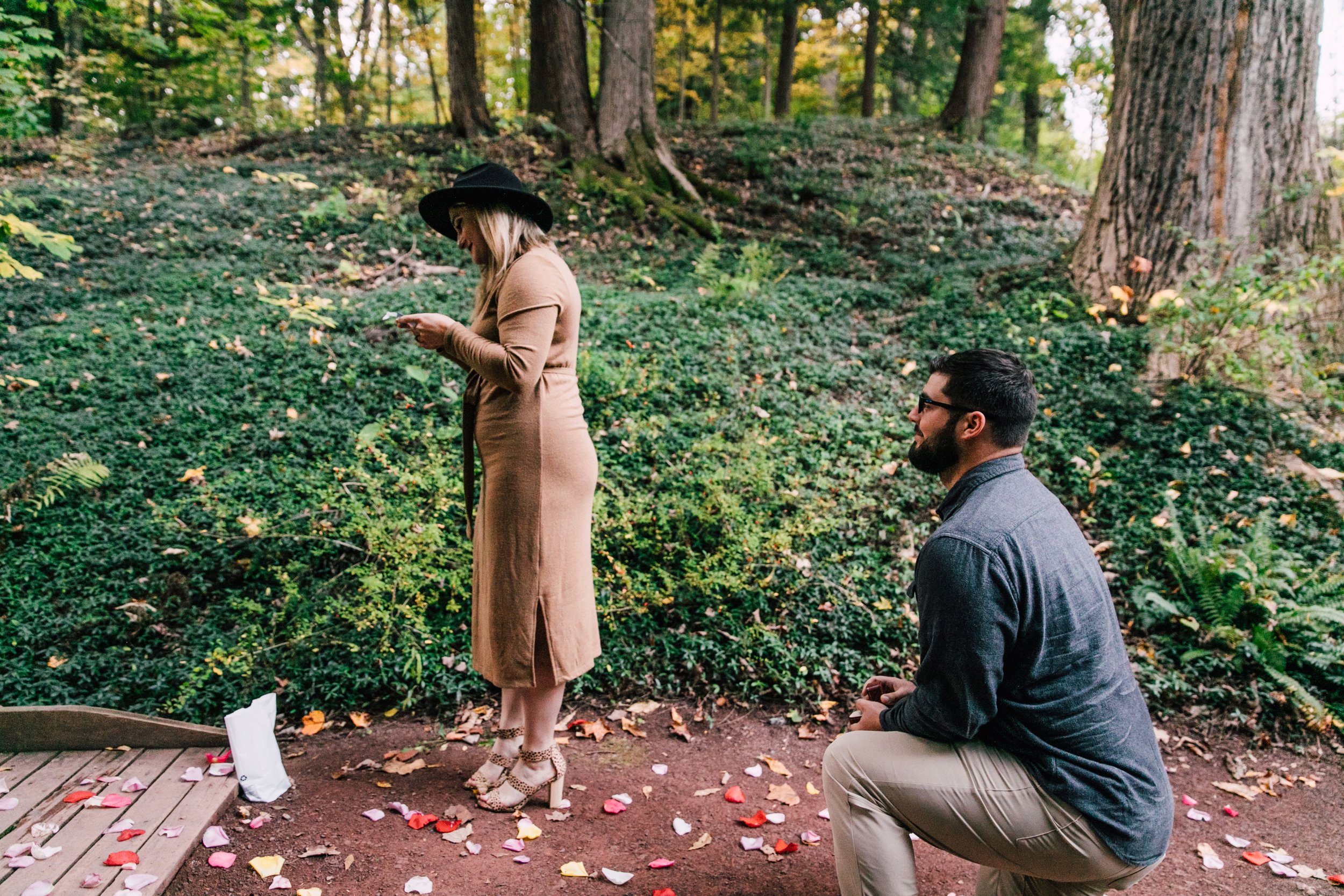  marissa reads a slip of paper as dustin waits eagerly behind her on one knee at their surprise proposal 