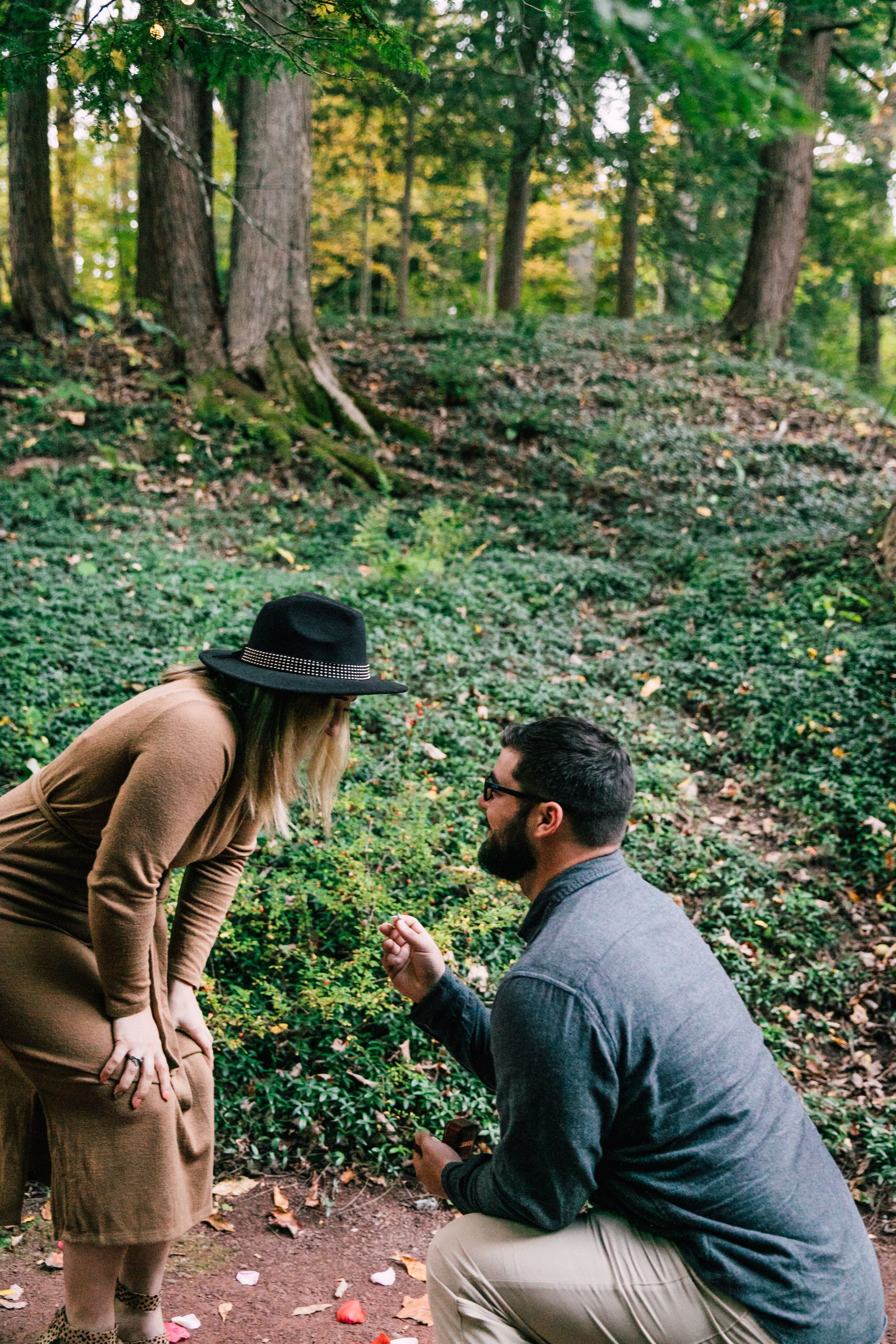  marissa rests her arms on her knees as she bends down towards her proposing boyfriend while central ny proposal photographer captures it all 