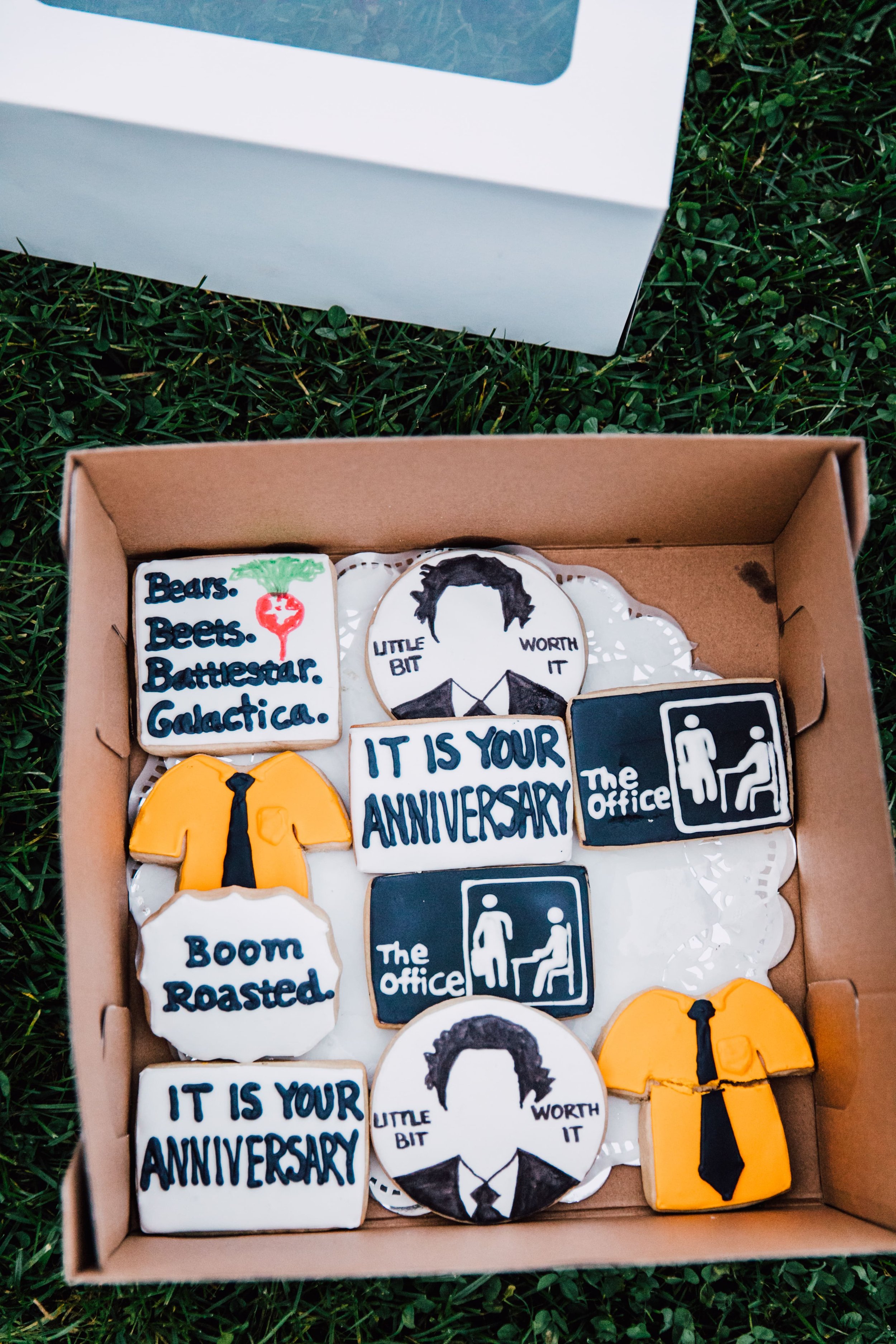  a box of the office themed cookies rest in the grass after a surprise proposal at root glen 