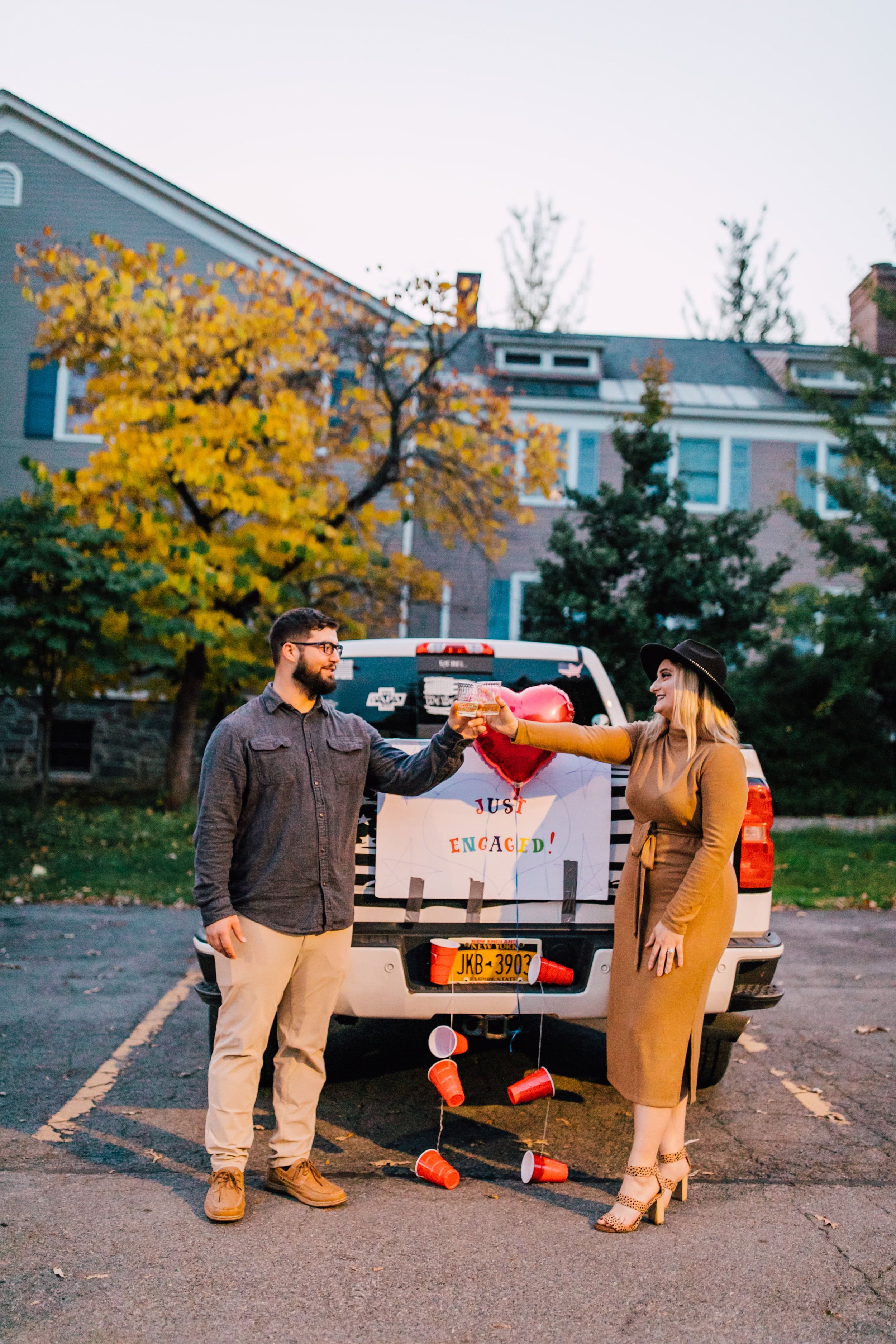  an engaged couple toasts in the parking lot as they celebrate their surprise proposal photography 