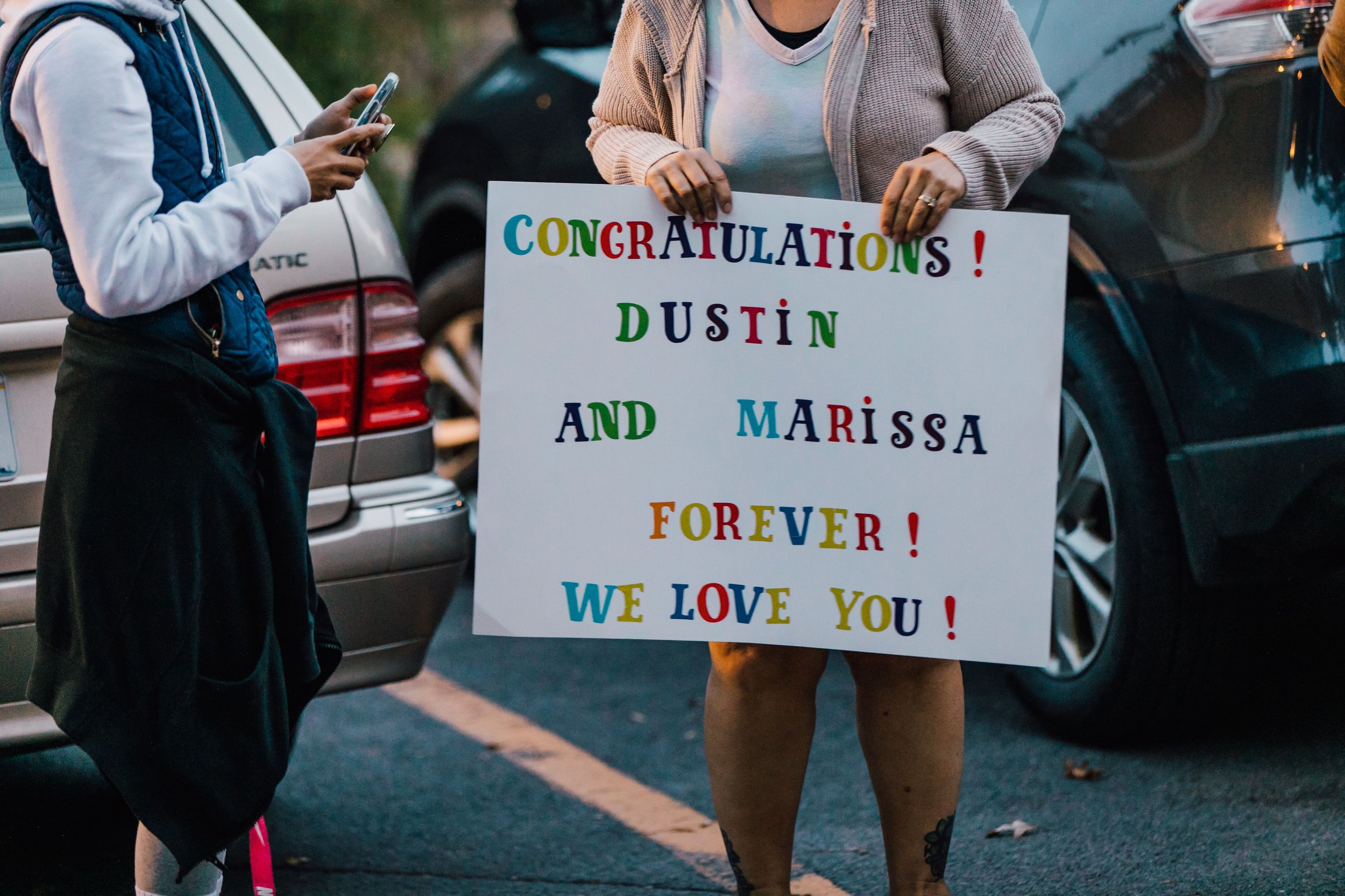  a family member holds a sign that reads “congratulations! Dustin and Marissa forever! We love you!” after surprise proposal photos 