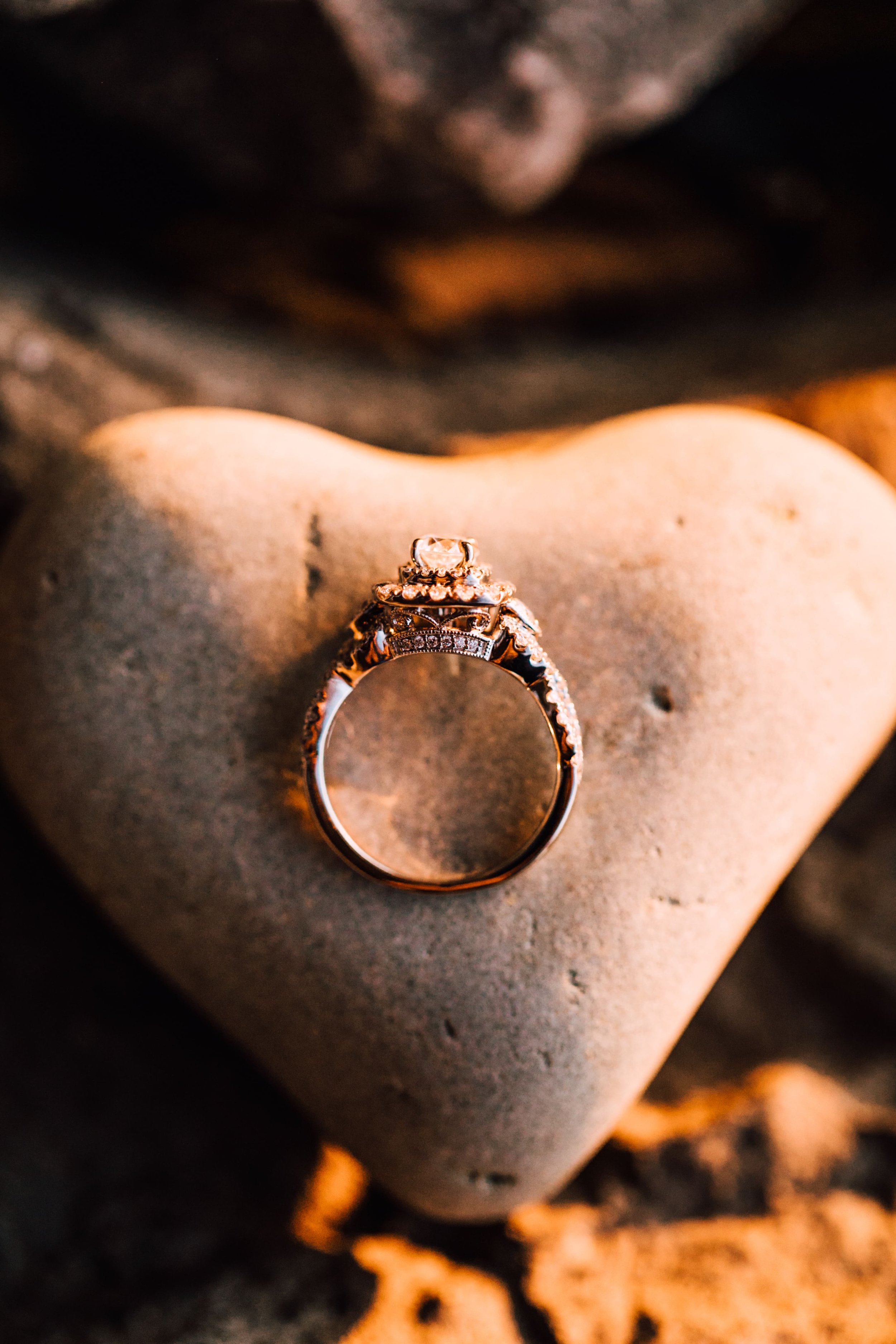  an engagement ring rests on a heart shaped rock in golden light during sunset engagement photos in central ny 