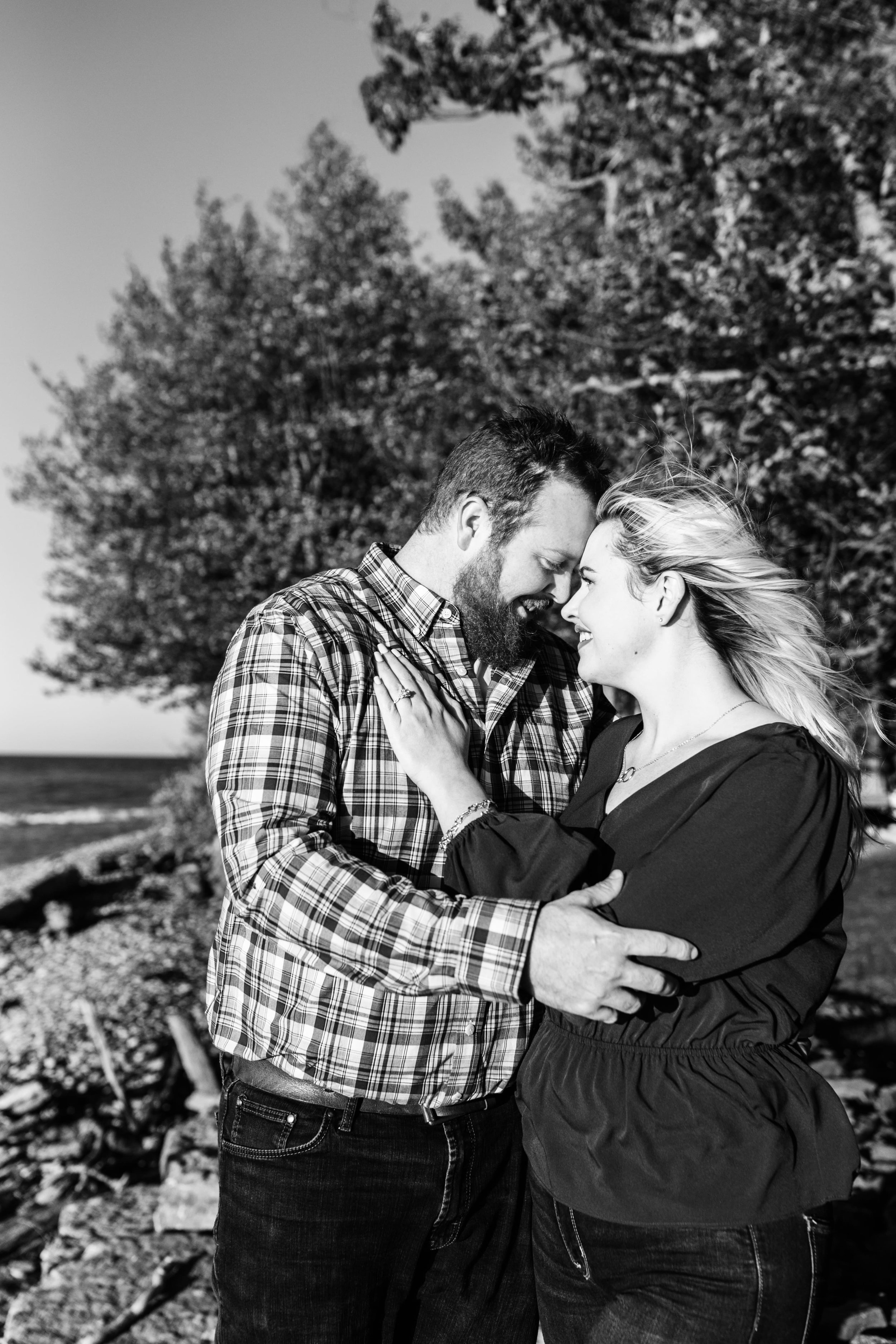  engaged couple presses their faces together as the wind blows back danielle’s hair during their lake engagement photos a one of the great lakes 
