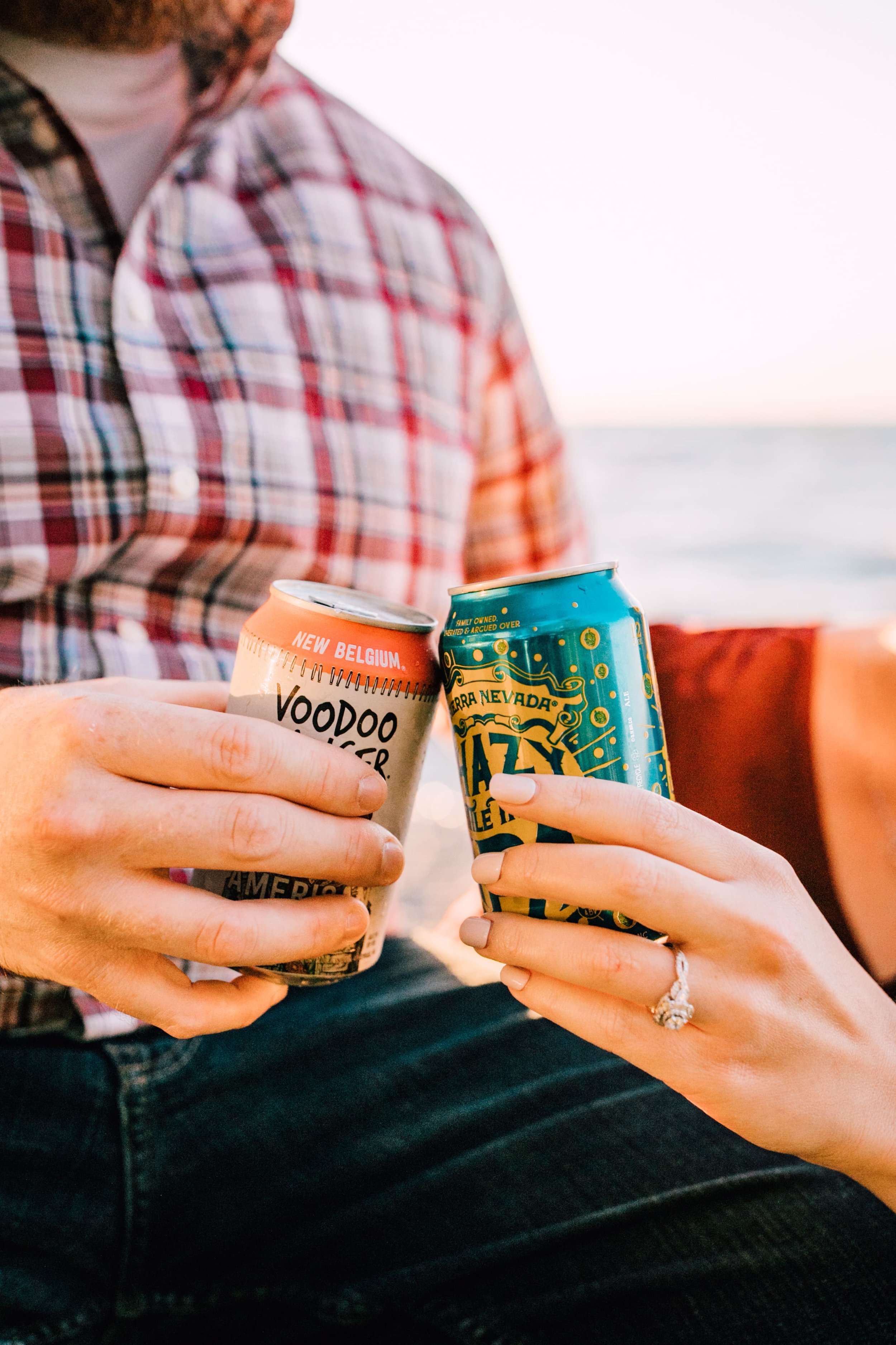  engaged couple show off the engagement ring as they cheers with local ipas during their sunset engagement photos on the shore of one of the great lakes 