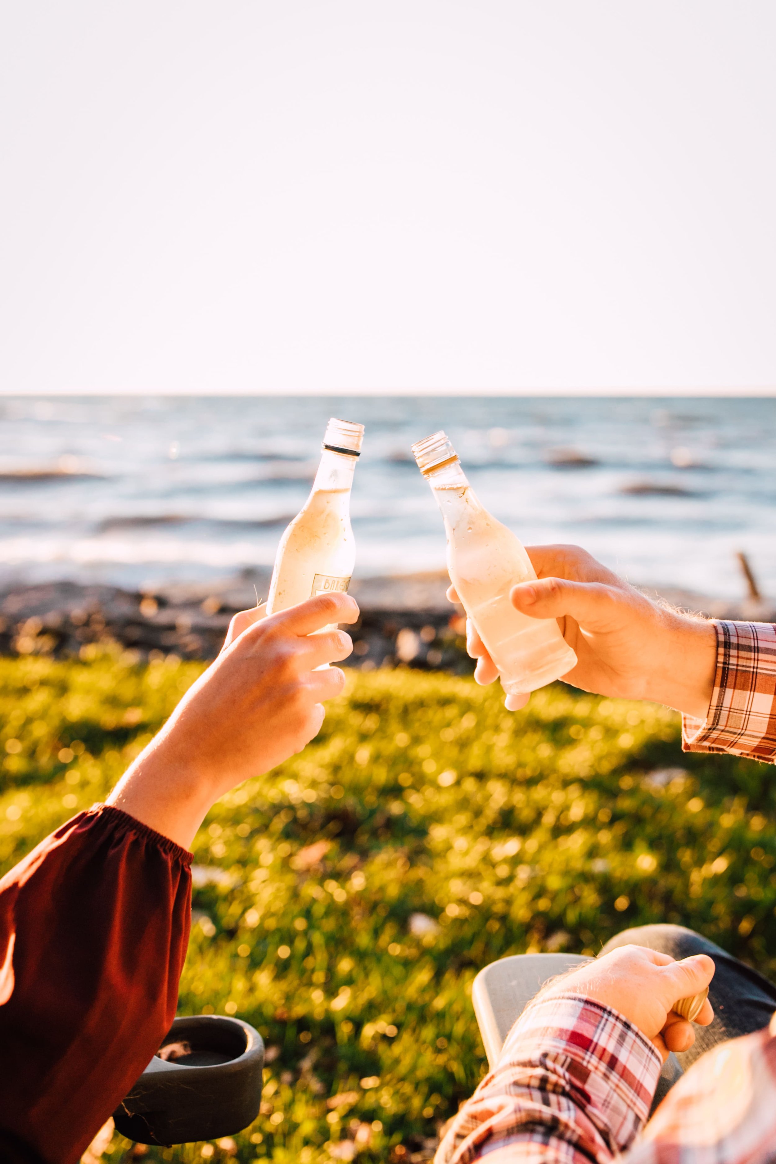  engaged couple toasts with wine coolers as they sit in adirondack chairs on the shore of a great lake during their sunset engagement photos  