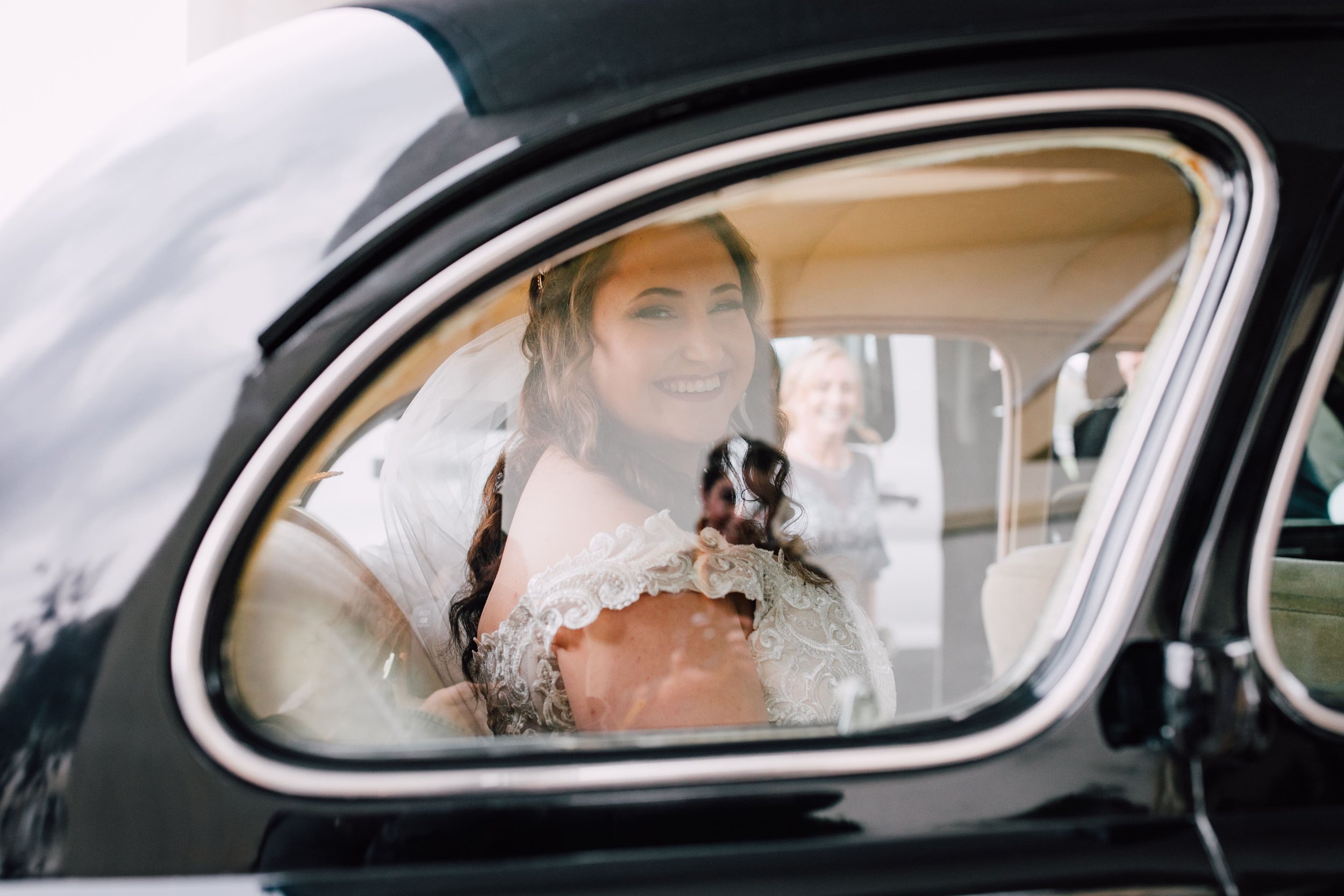  the bride smiles from the inside of her grandfather’s vintage car on the way to her fall wedding ceremony 