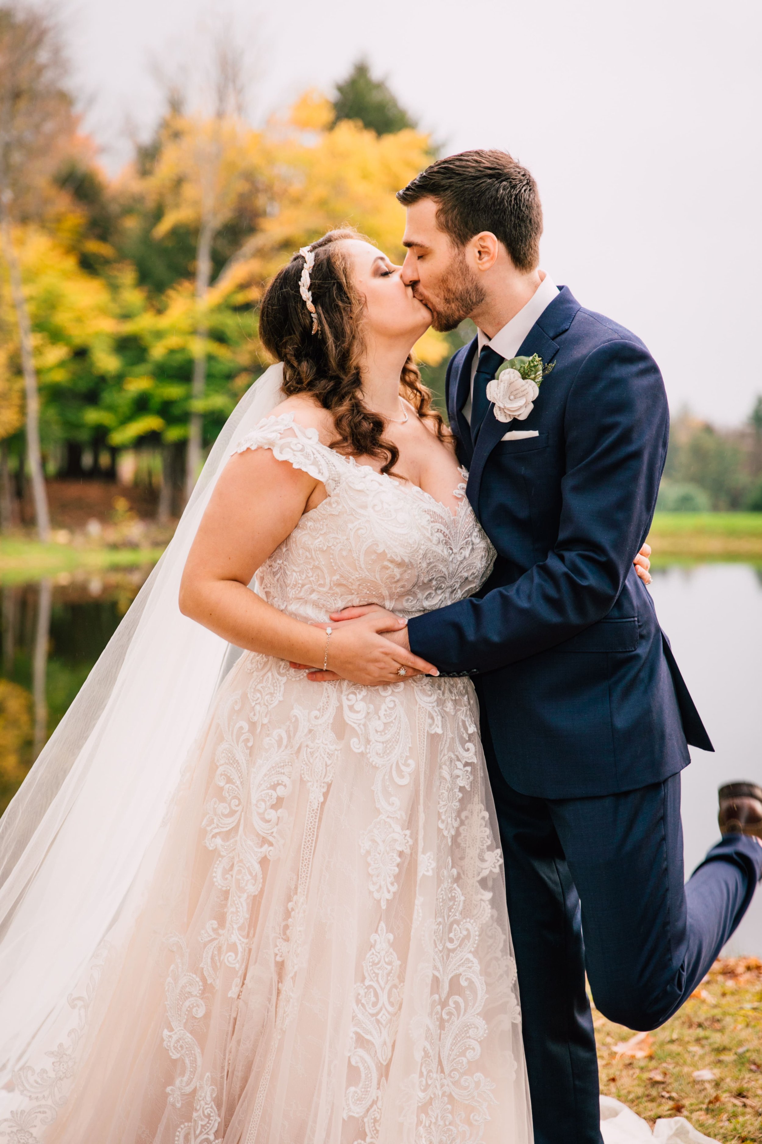  the bride and groom share a kiss as the groom pops his foot during their fall wedding photos 