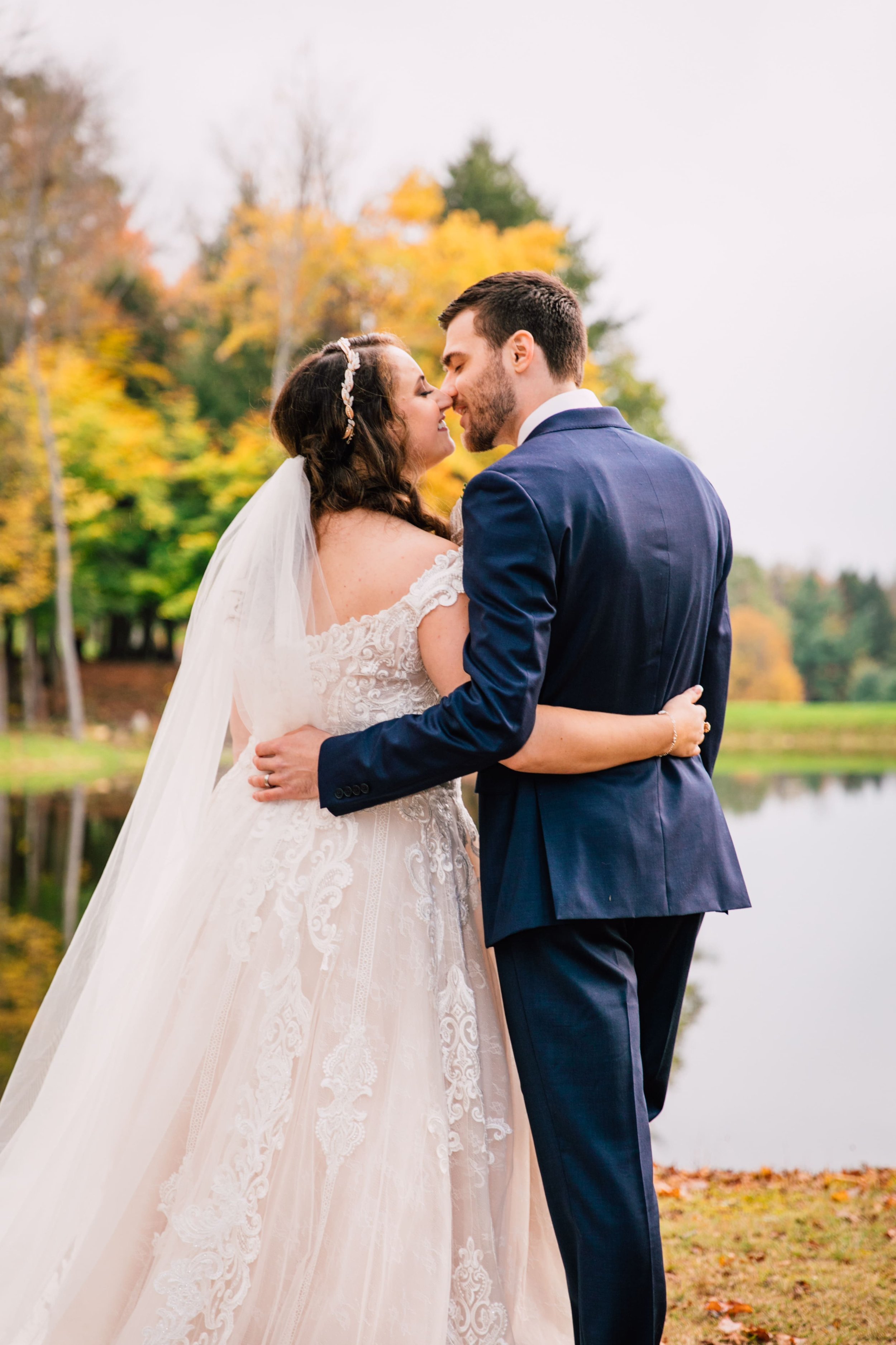  the bride and groom lean in for a kiss with their arms wrapped around each others backs while taking fall wedding photos 