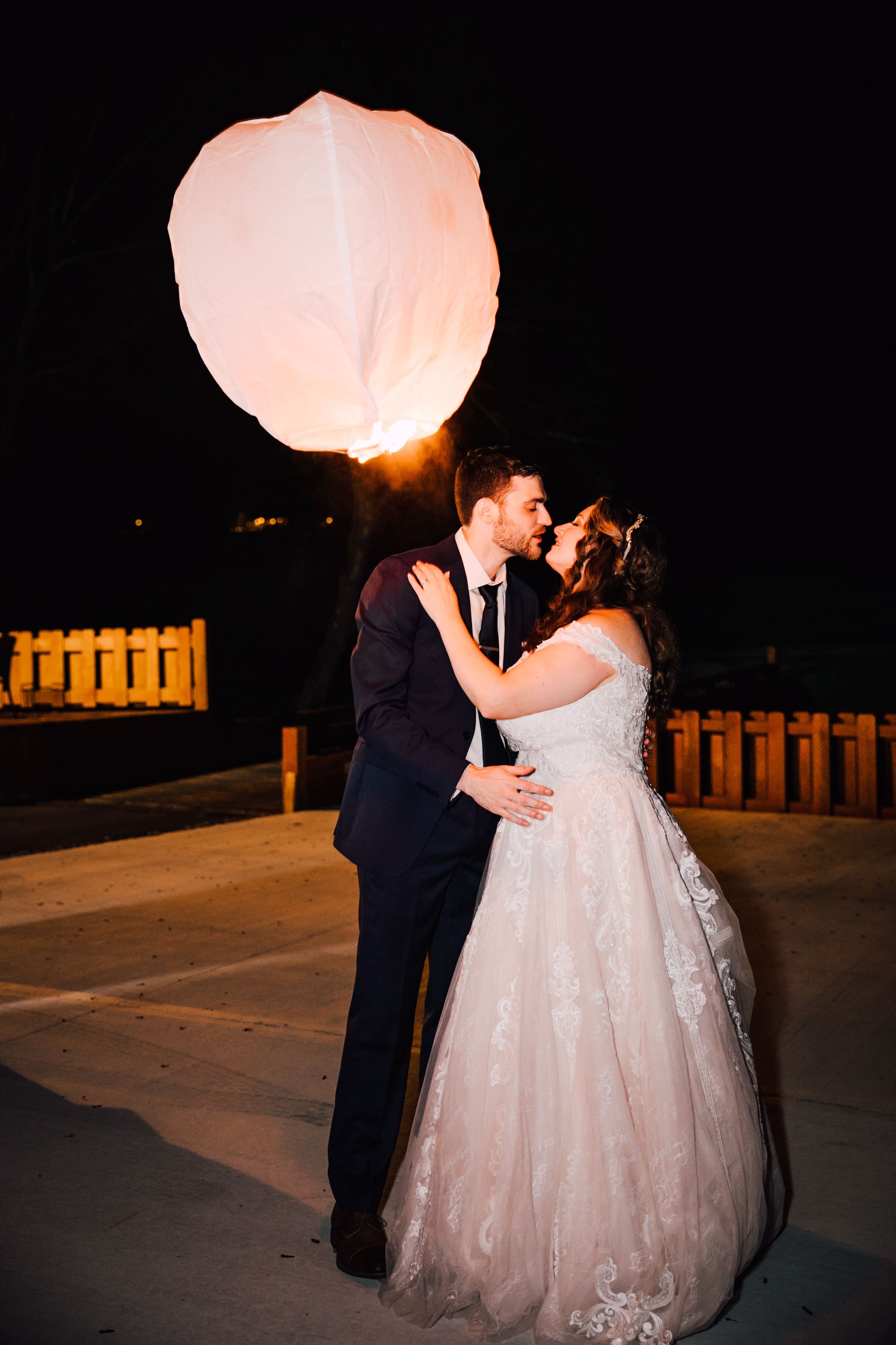  the bride and groom lean in for a kiss during night portraits as a paper lantern flies off behind them during their book themed wedding 