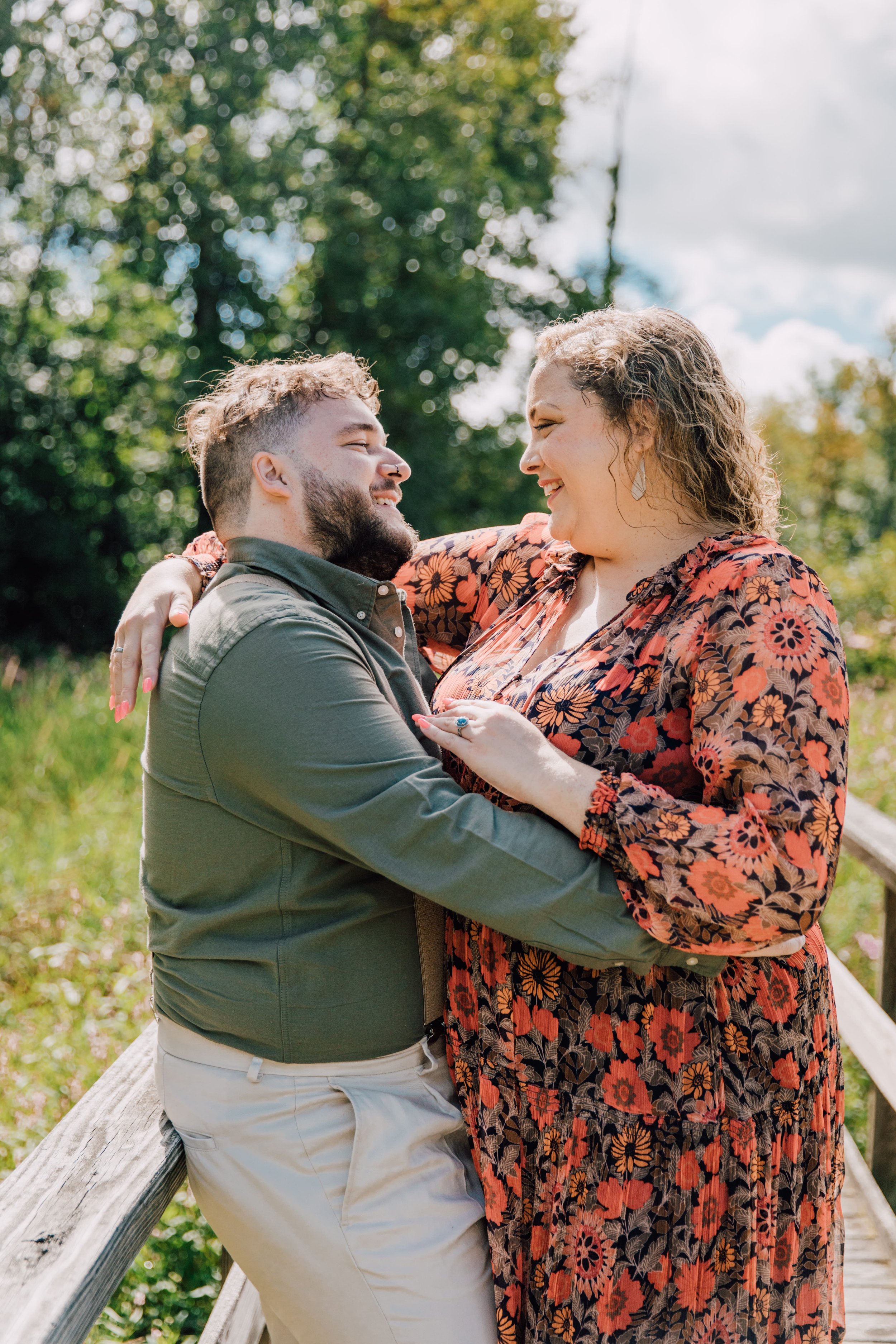  engaged couple stand in an embrace on a wooden bridge while central new york photographer takes their engagement photos at rice creek field station 