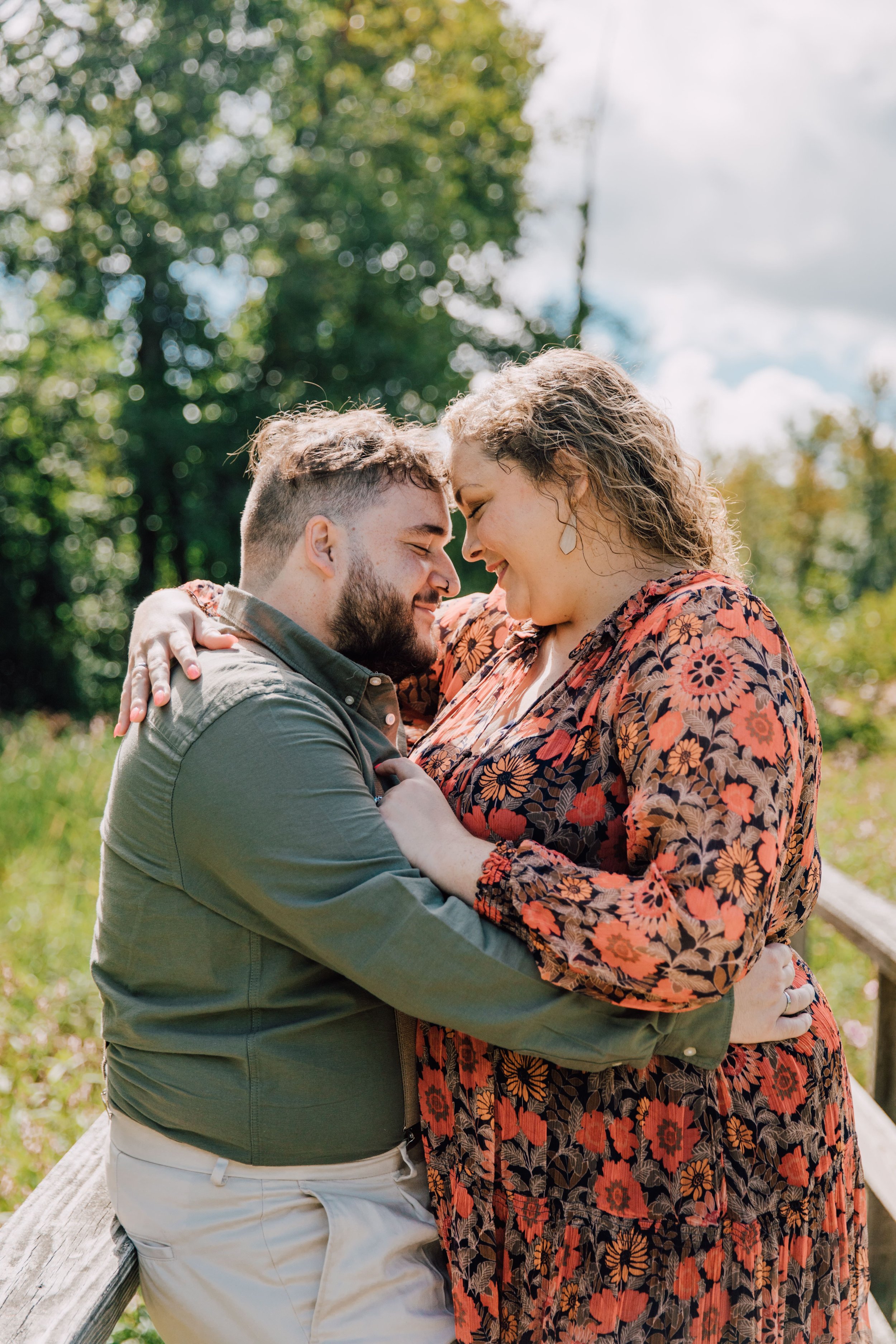  engaged couple lean their faces together while in an embrace while standing on a bridge while central new york photographer captures their forest engagement photos 