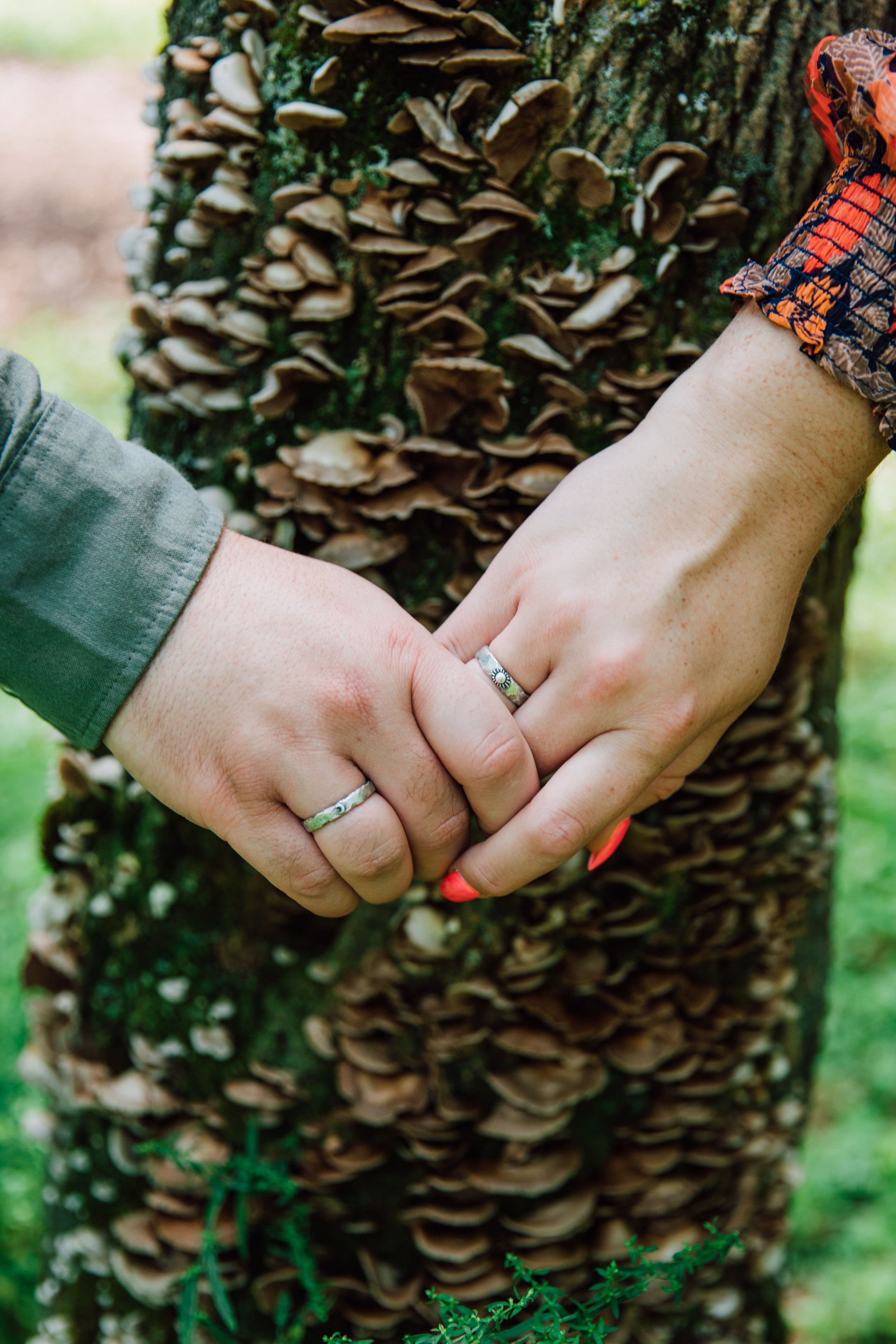 engaged couple shows their matching sun and moon rings in front of a growing mushroom during their engagement session at rice creek field station 