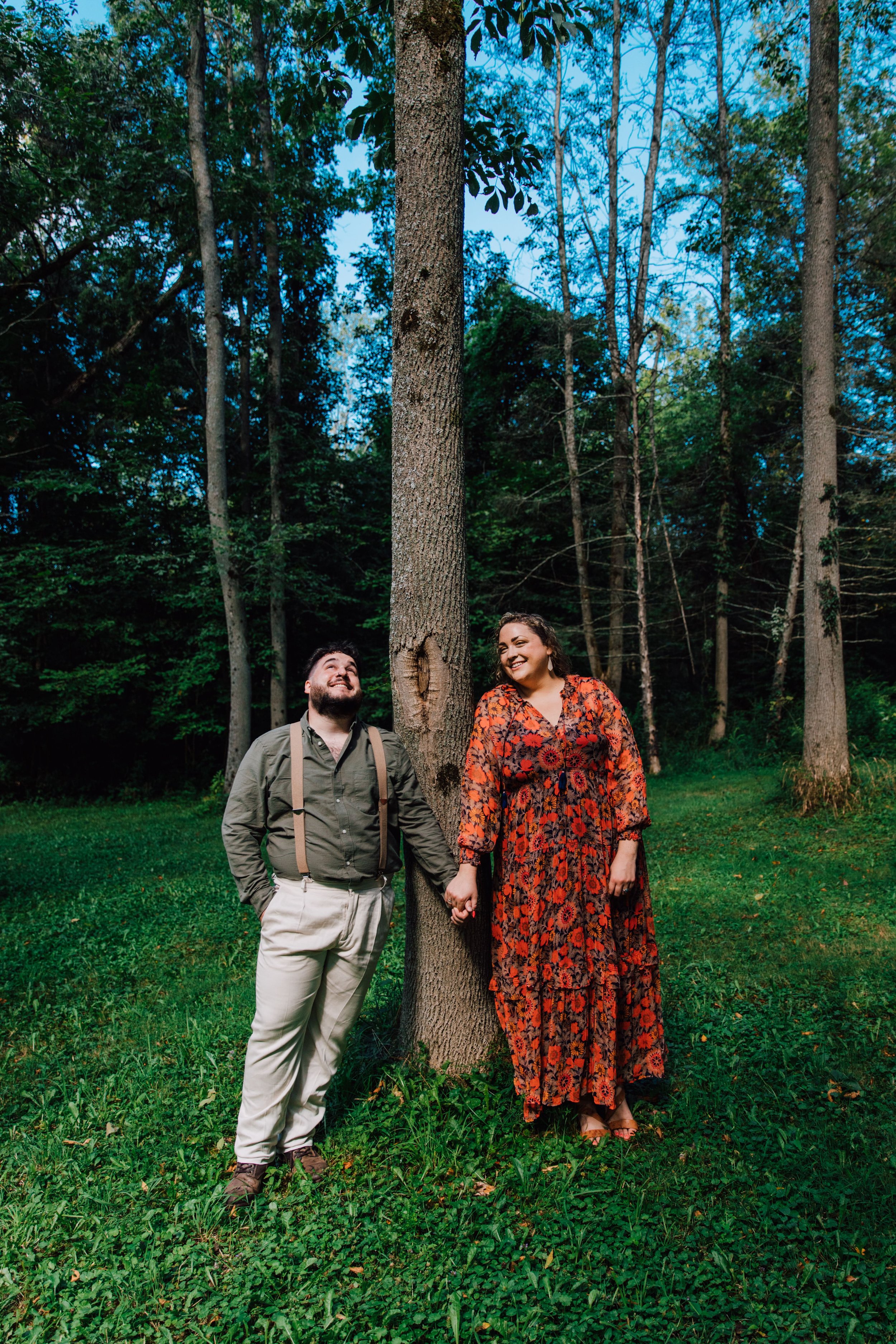 an engaged couple hold hands as they lean on a thin tree during their forest engagement photos 