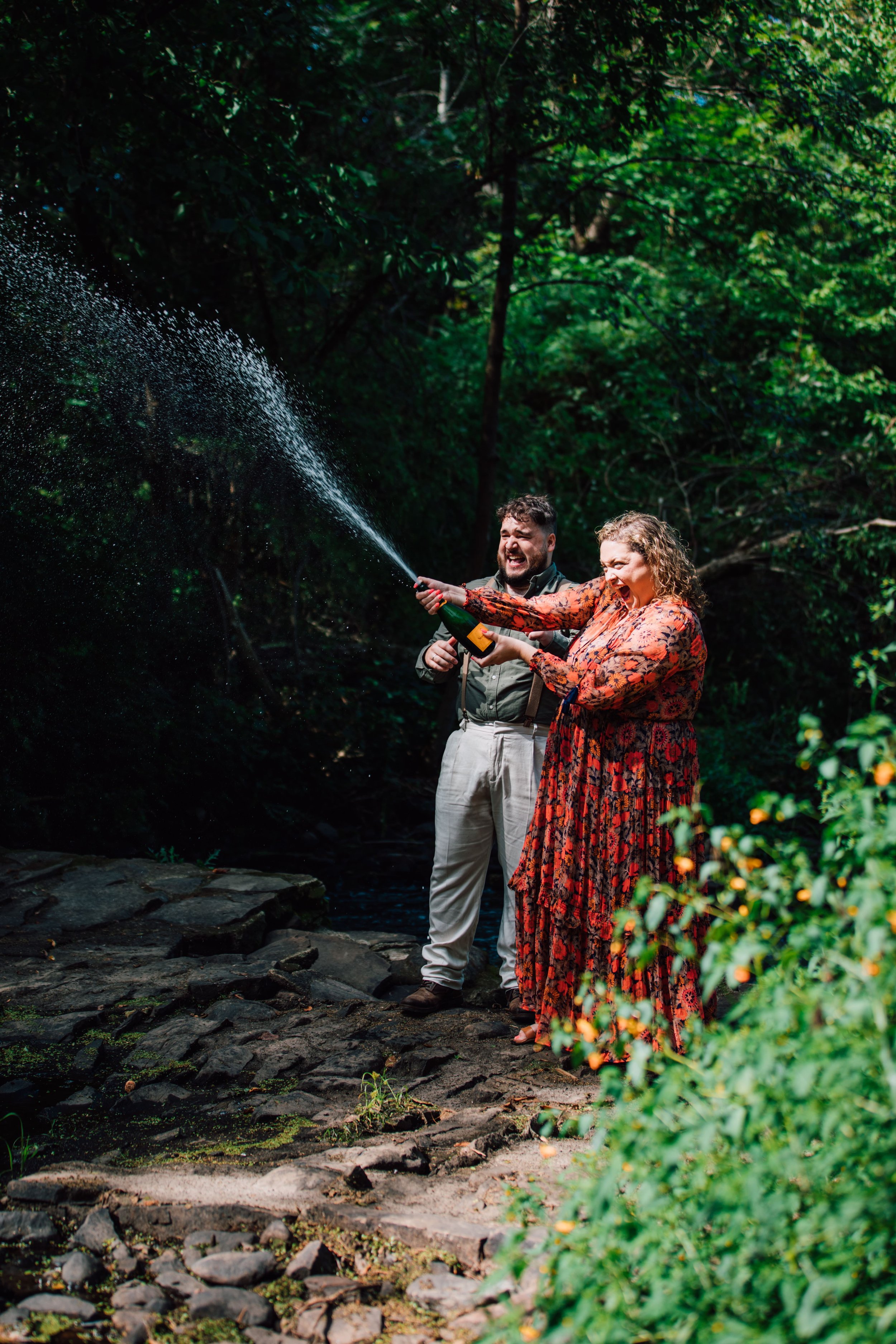  an engaged couple do a champagne pop during their engagement photos in the woods 