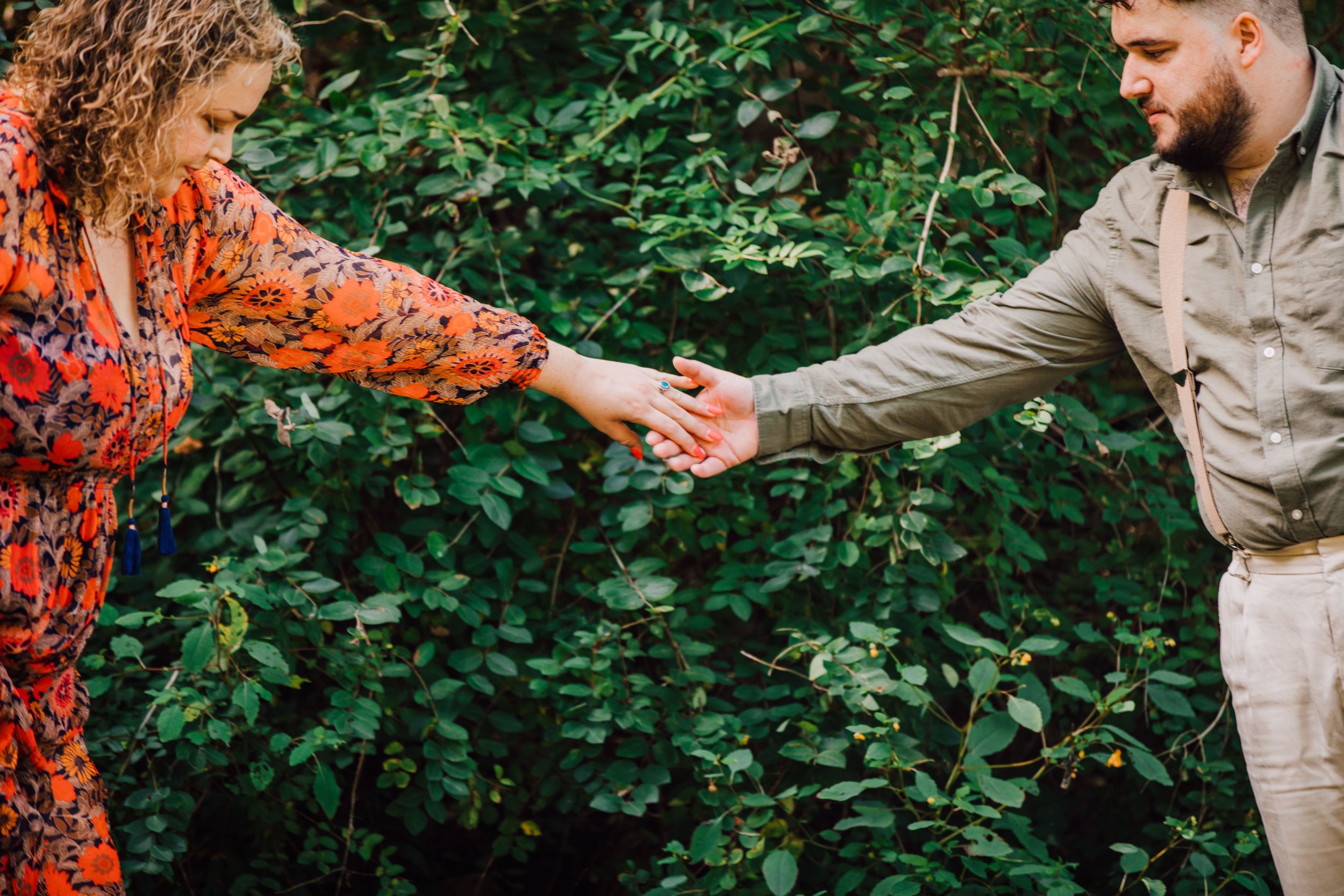  matt grabs his fiancee’s hand to help her over the creek at rice creek field station during their engagement session 