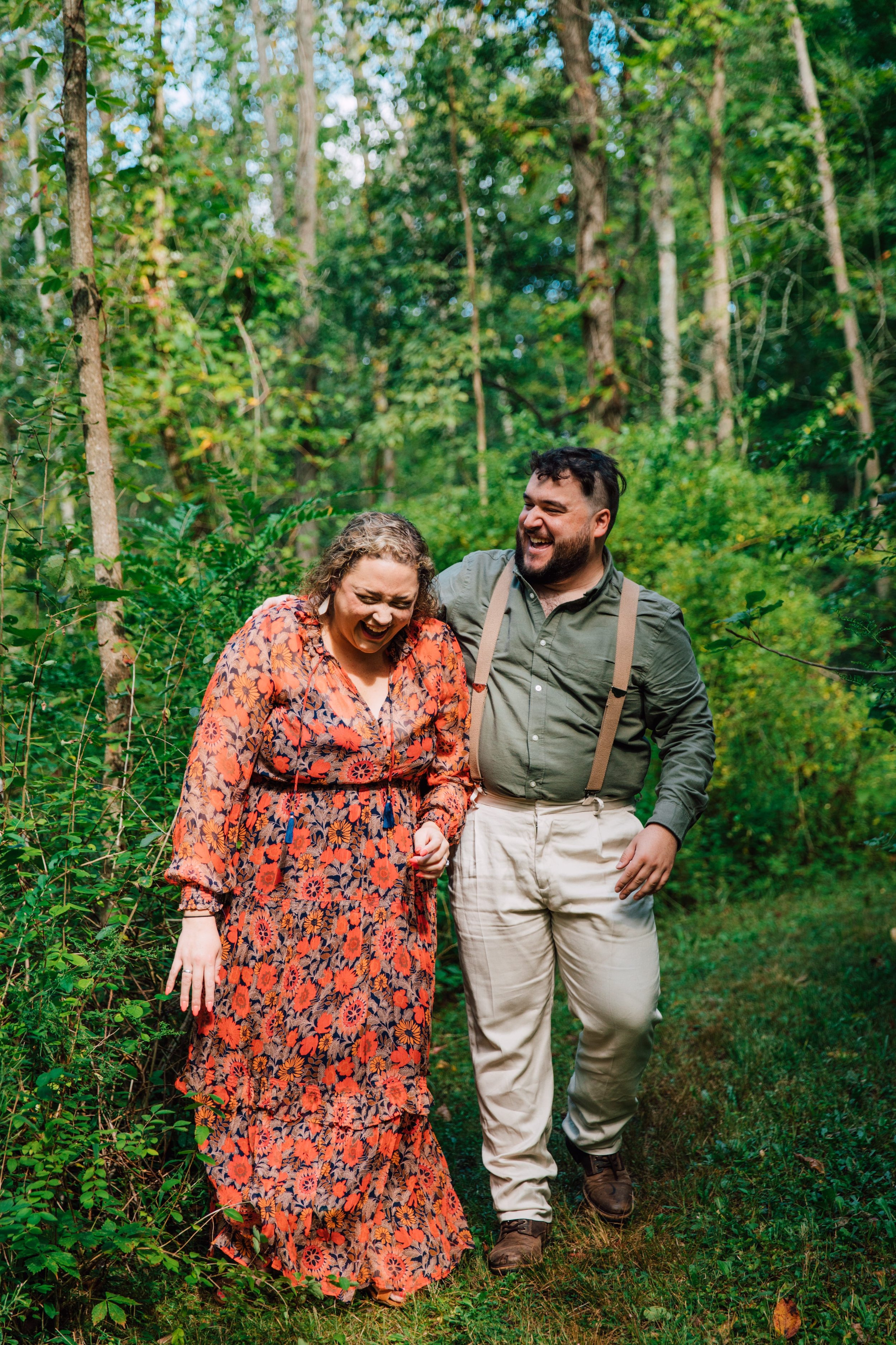  an engaged couple laugh as they walk together while taking their forest engagement photos 
