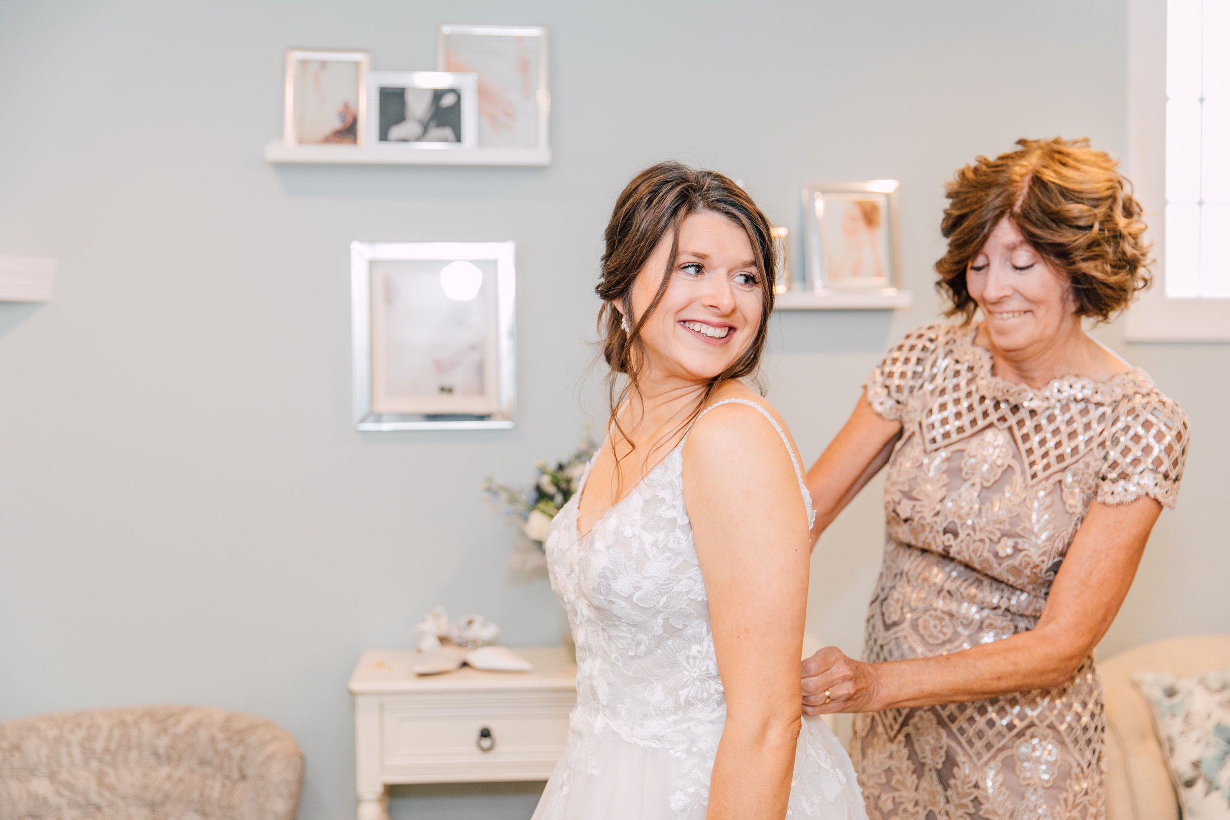  the bride smiles as her mother gets her dress buttoned up before her rustic fall wedding 