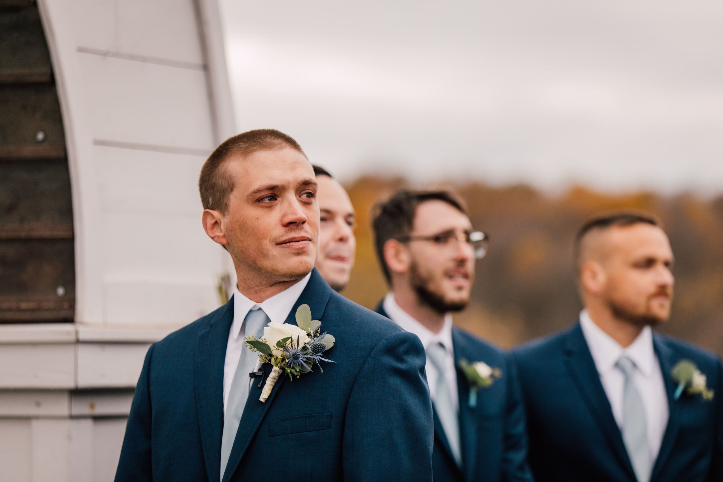  the groom looks thoughtfully out as he holds back tears as he watches the bride walk down the aisle at their outdoor fall wedding 