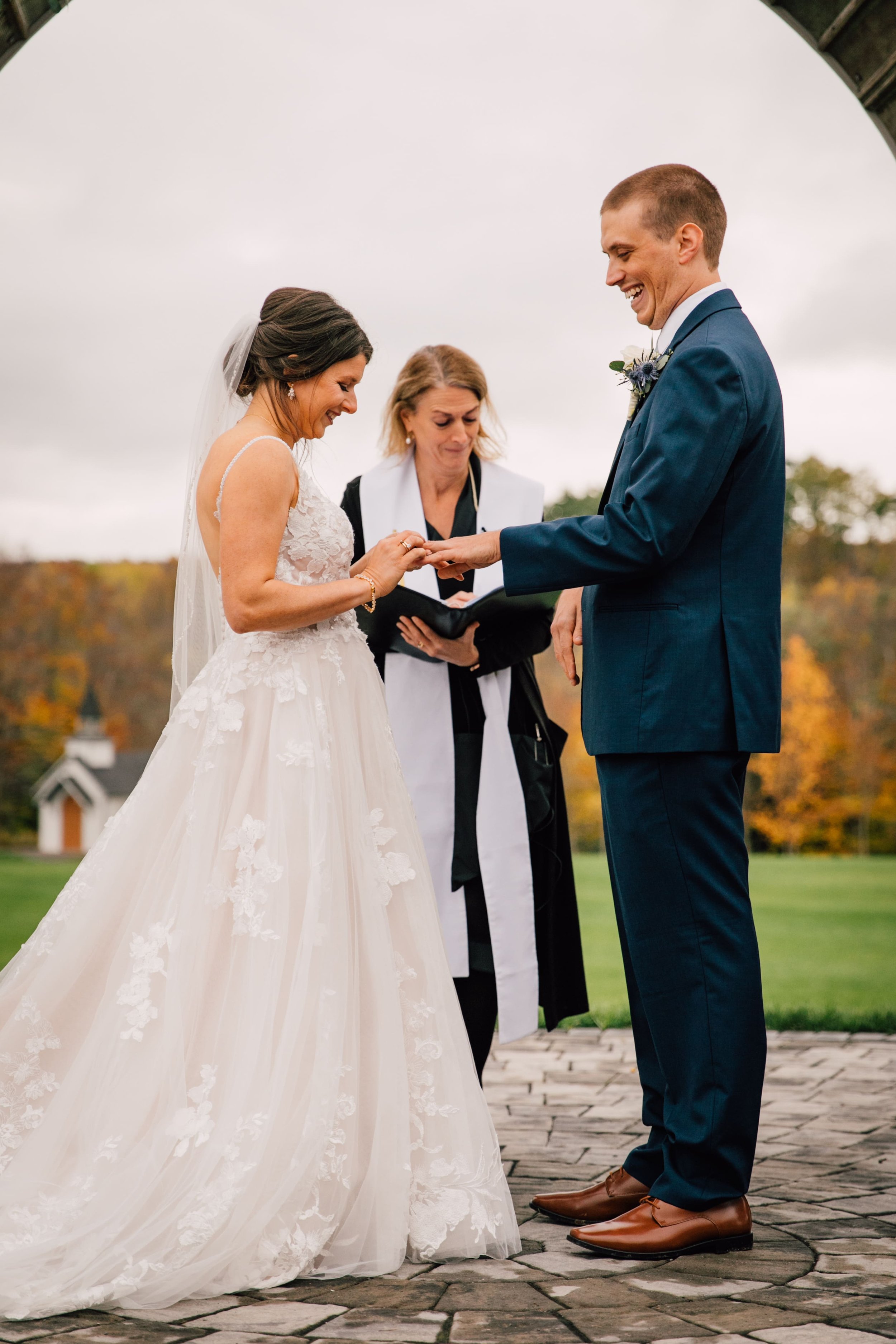  the bride puts the grooms ring on his finger during their outdoor fall wedding ceremony 