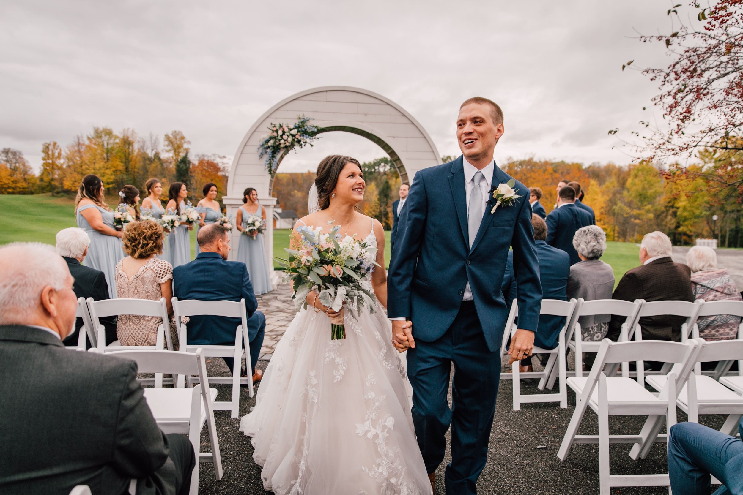  the bride and groom beam as they walk down the aisle together after their outdoor fall wedding 
