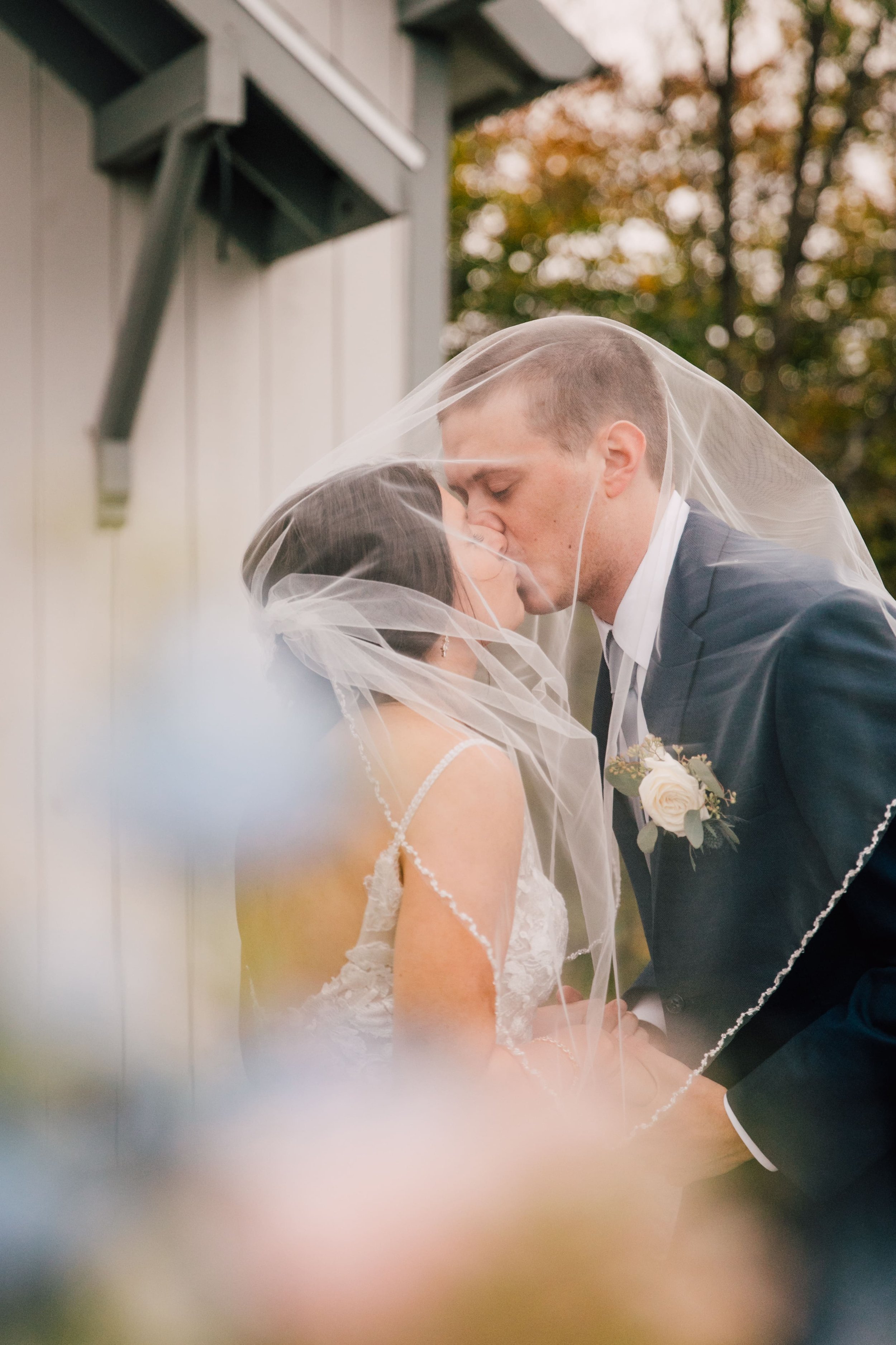  the bride and groom kiss under her veil while posing for fall wedding photos 