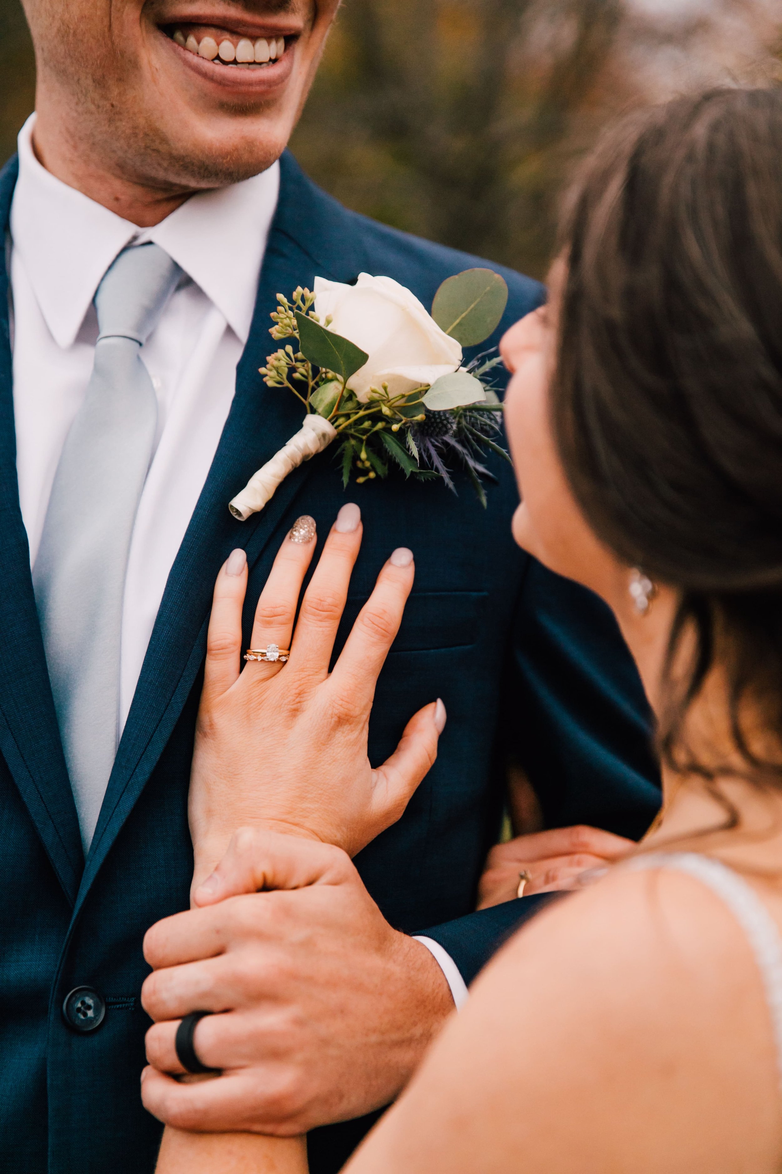  the bride and groom smile as she rests her hand on his chest and he holds her arm to show their new wedding rings after their rustic fall wedding 