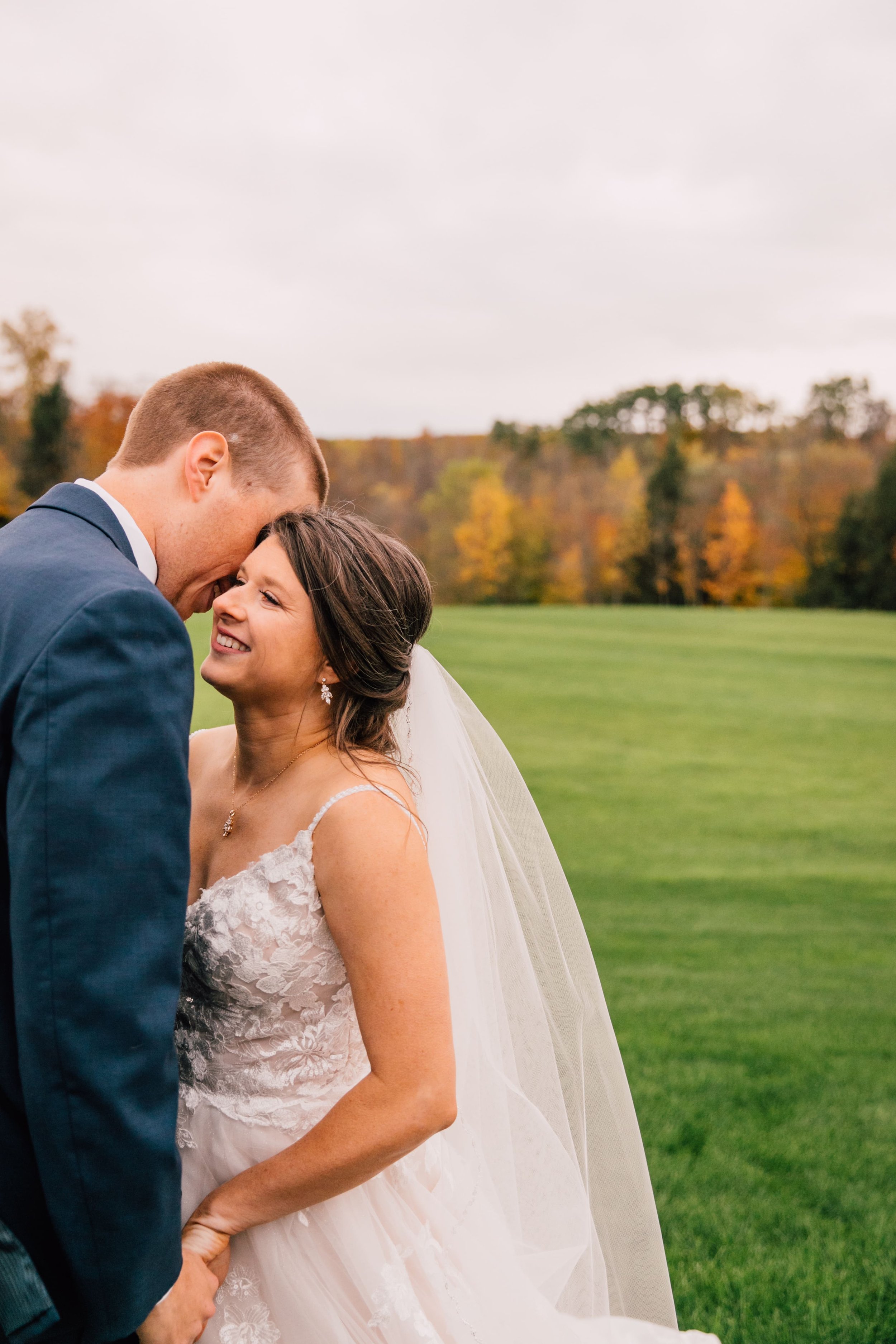  the groom presses his forehead to the side of the bride’s face as she smiles during their fall wedding photos 