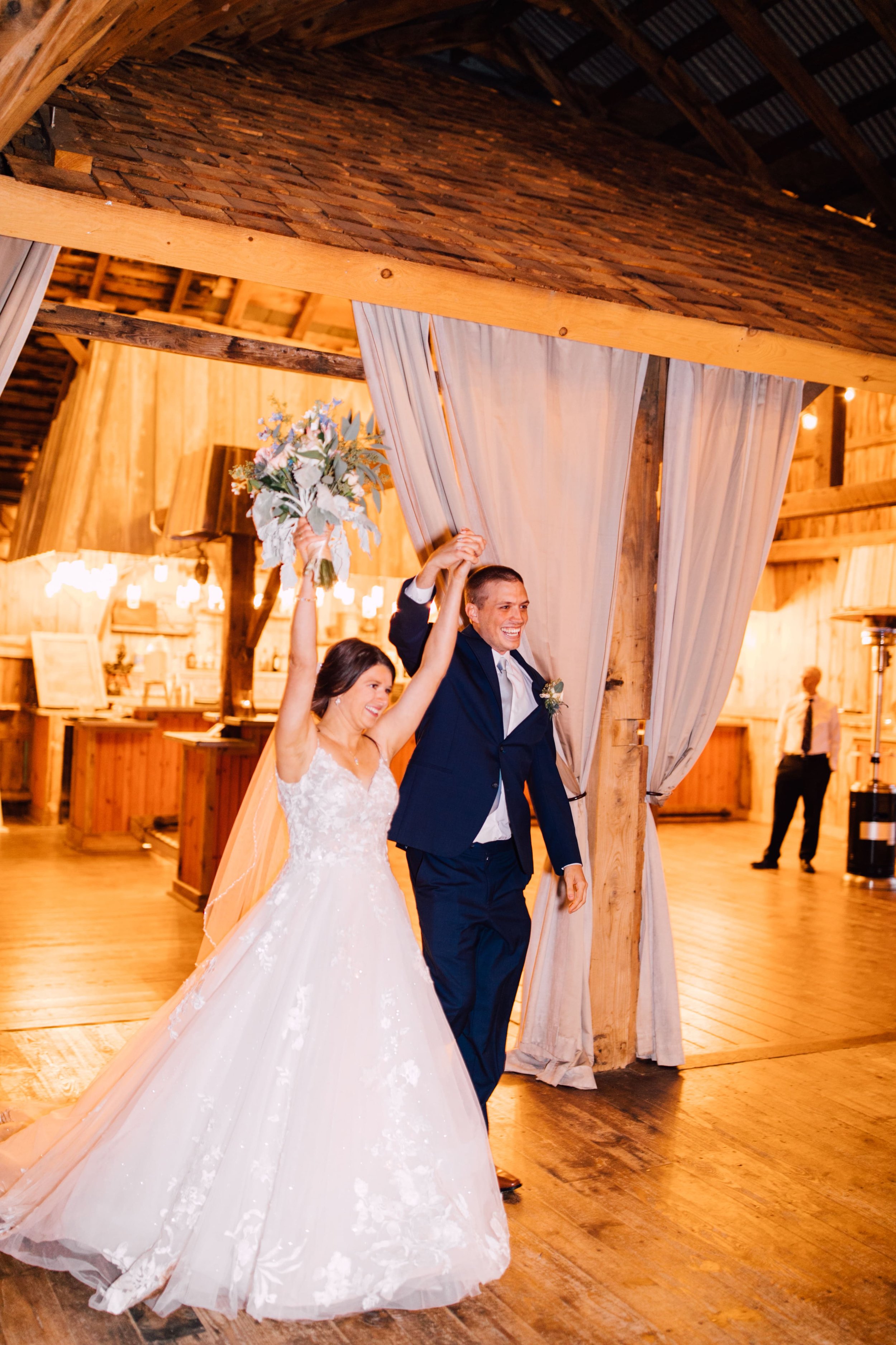  the bride and groom walk into their reception with arms outstretched at their elegant barn wedding 