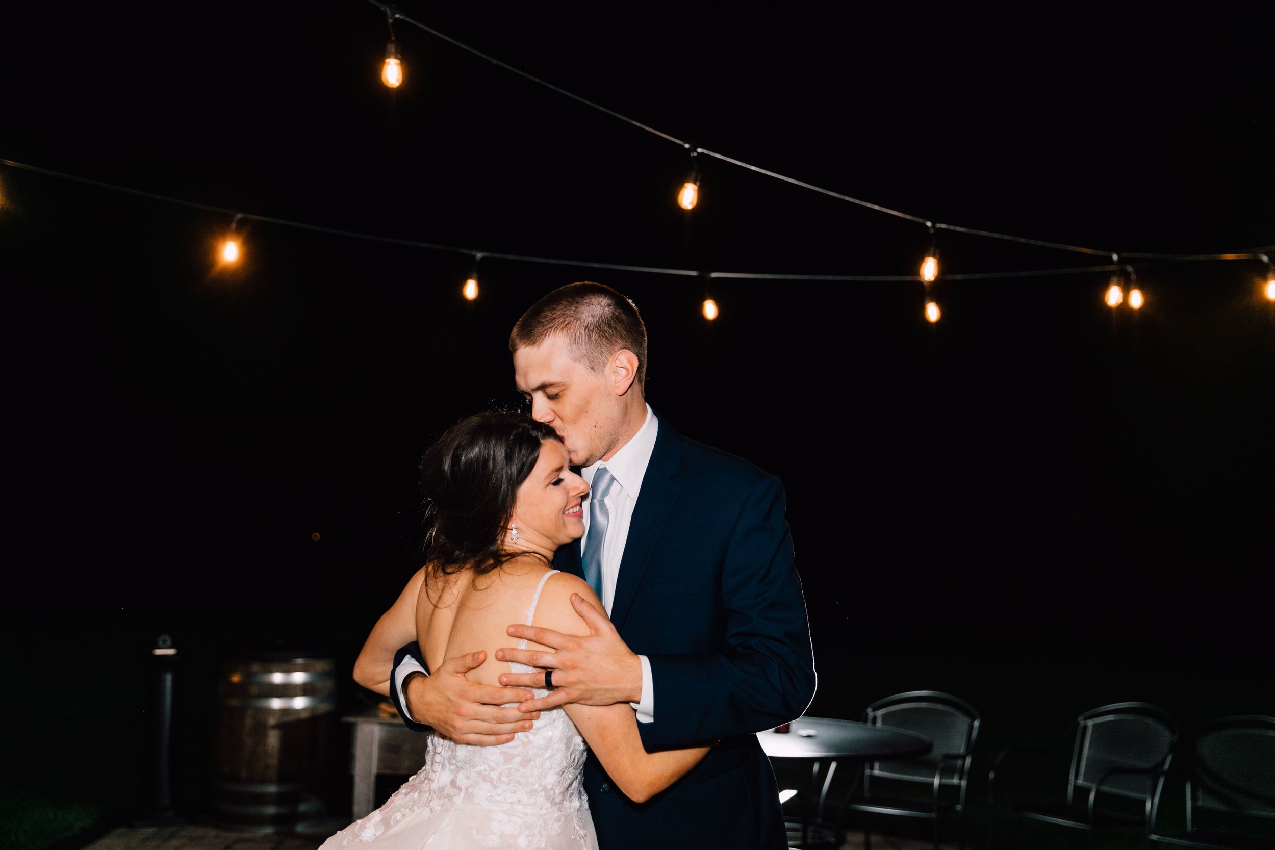  the groom kisses the bride on the forehead during night portraits at their outdoor fall wedding 