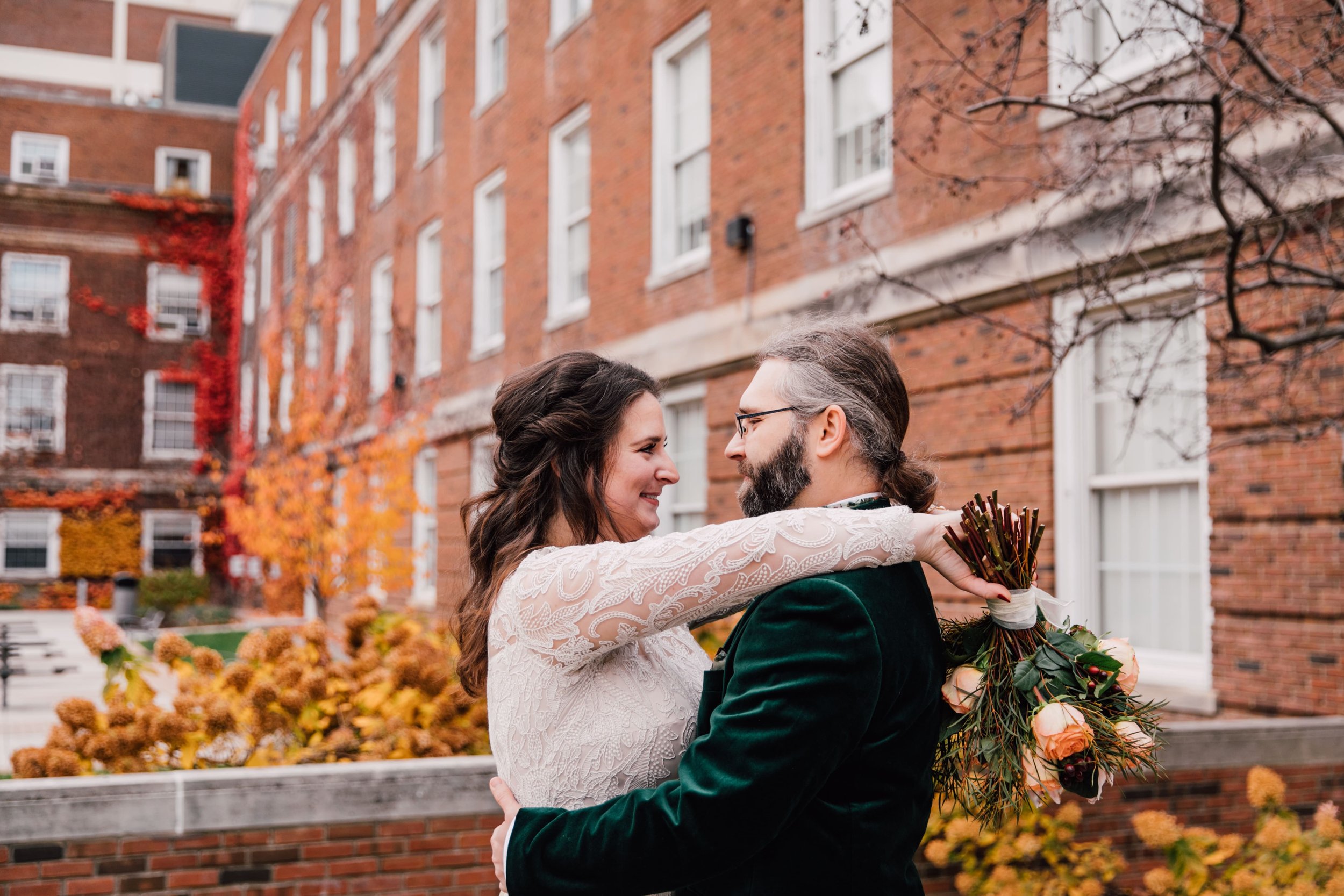  syracuse ny wedding photographer captures a couple gazing at each other, the bride rests her arms on the groom shoulder with her fall bouquet upside down in her hand 
