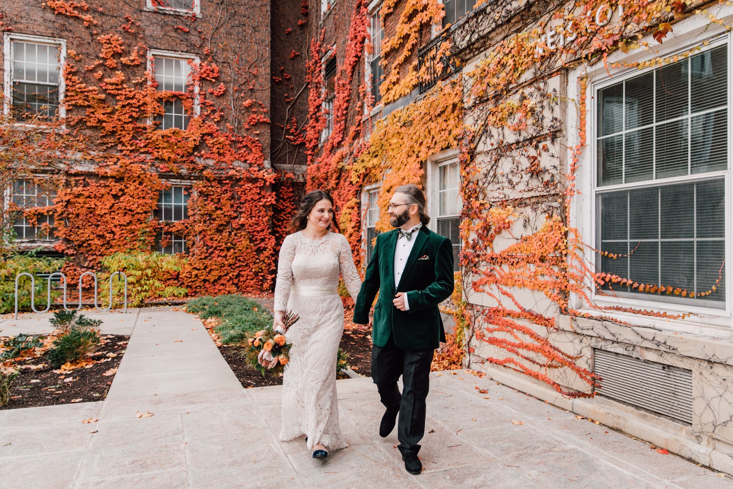  Syracuse Wedding Photographer captured a photo of the bride and groom walking toward her they hold hands with one hand and the bride holds her bouquet in the other while the groom rests his hand on his jacket button 