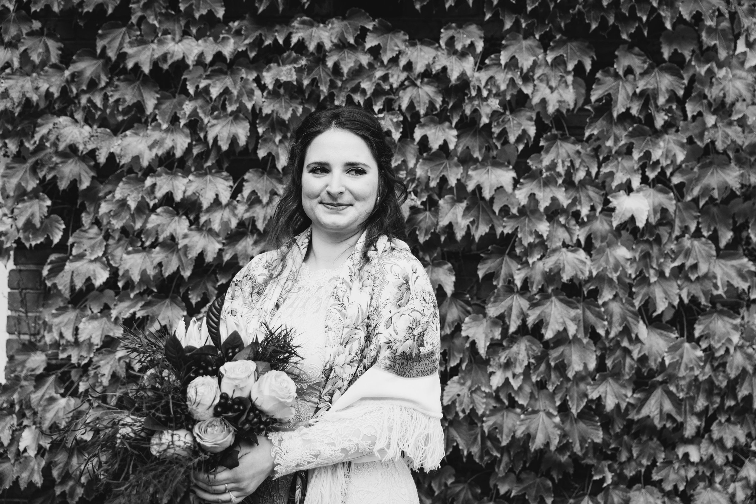  the bride holds her bouquet and smiles will looking to the side and standing in front of ivy while taking her syracuse wedding photography photos 