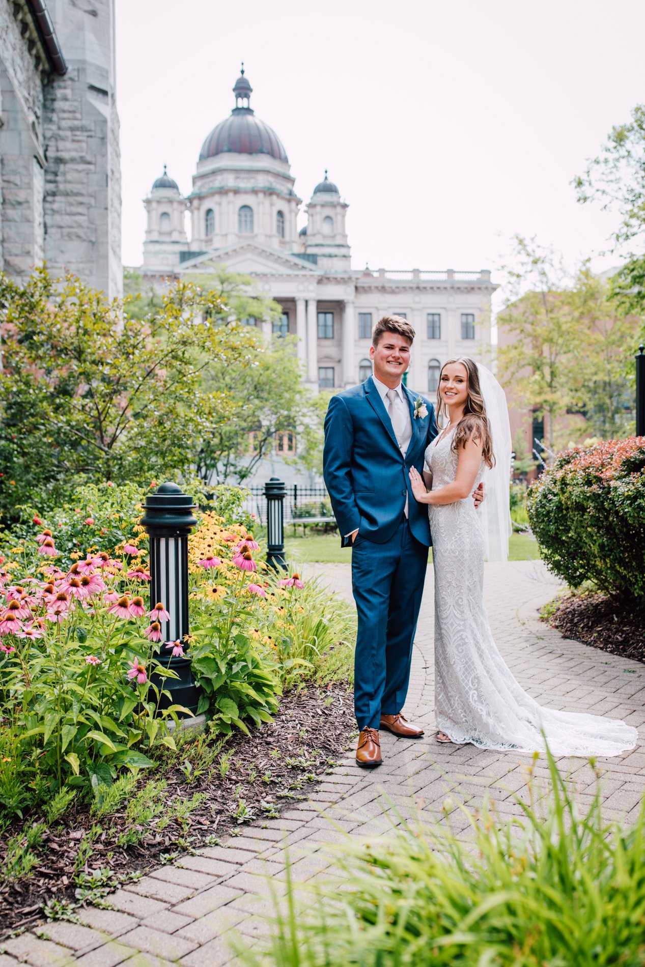 Bride and Groom smile while standing in a church garden during their traditional wedding in downtown Syracuse 