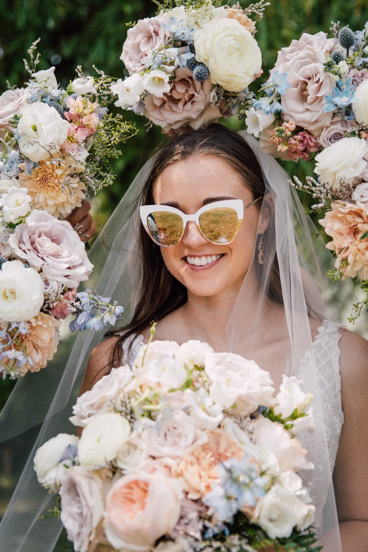  Bride wears sunglasses while bridesmaids hold their bouquets around her head 