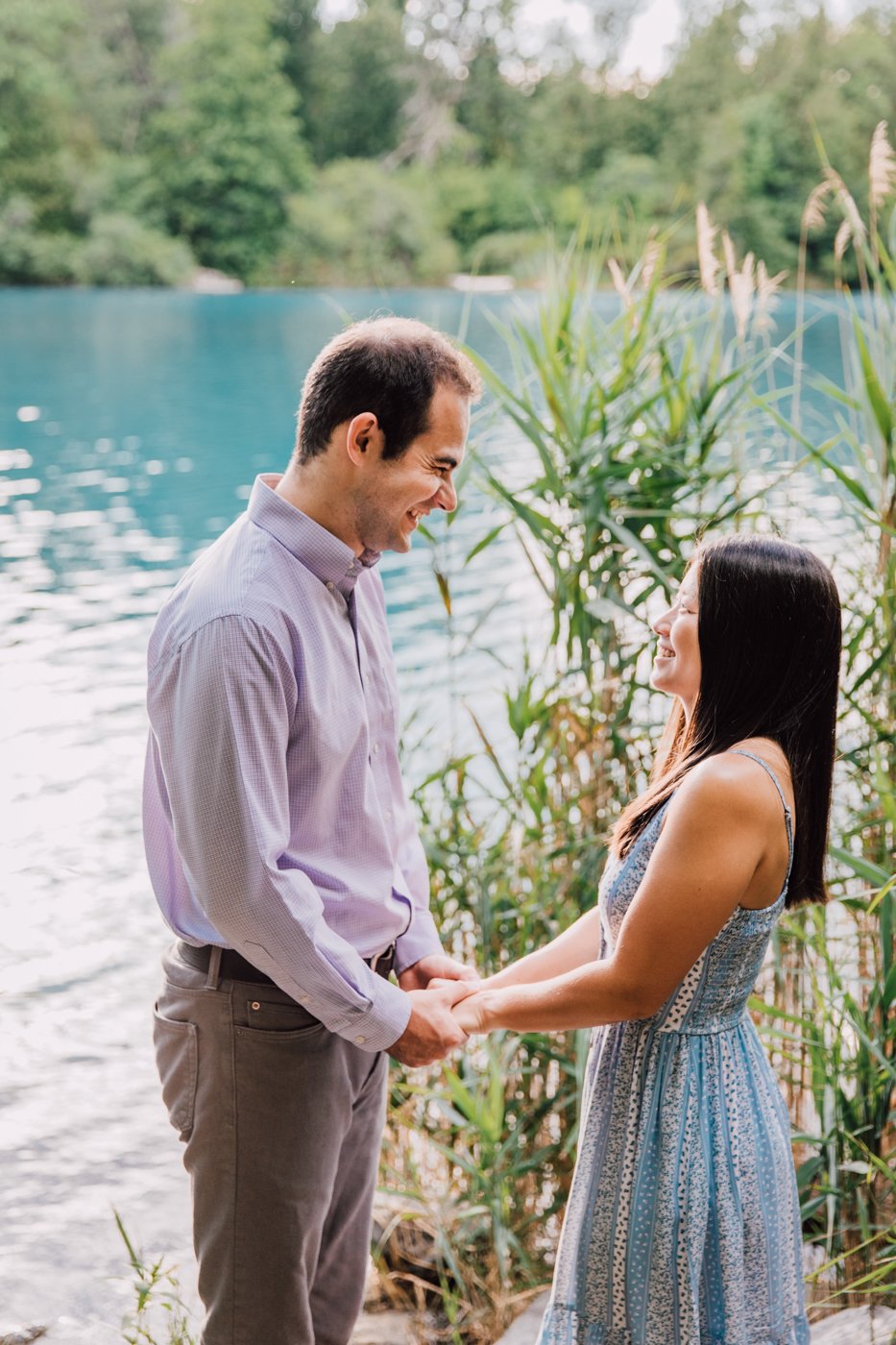  Engaged couple holds hands overlooking a lake during while having engagement photos taken at Green Lakes State Park in Fayetteville, NY   