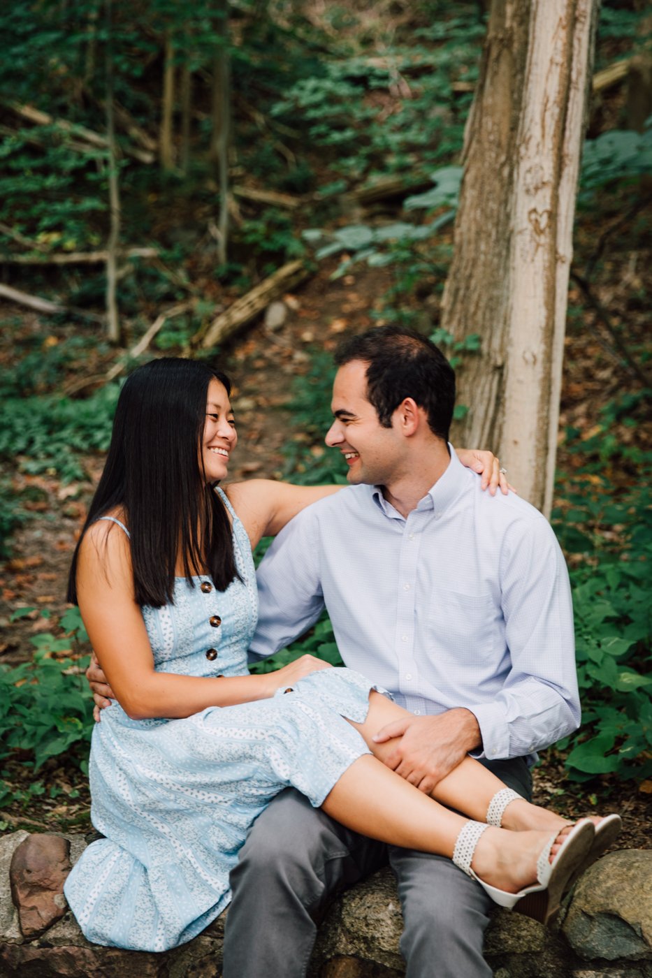  Woman sits on her fiances lap during forest engagement photos at Green Lakes State Park 
