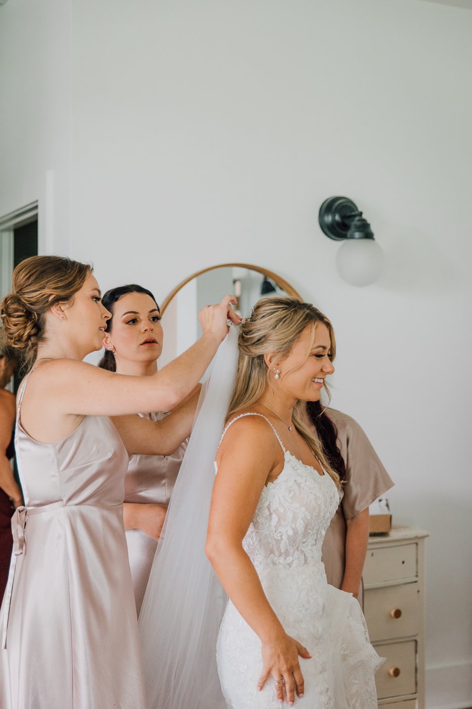  Bridesmaids put a Bride’s veil into her hair as she gets ready for her fingerlakes wedding 