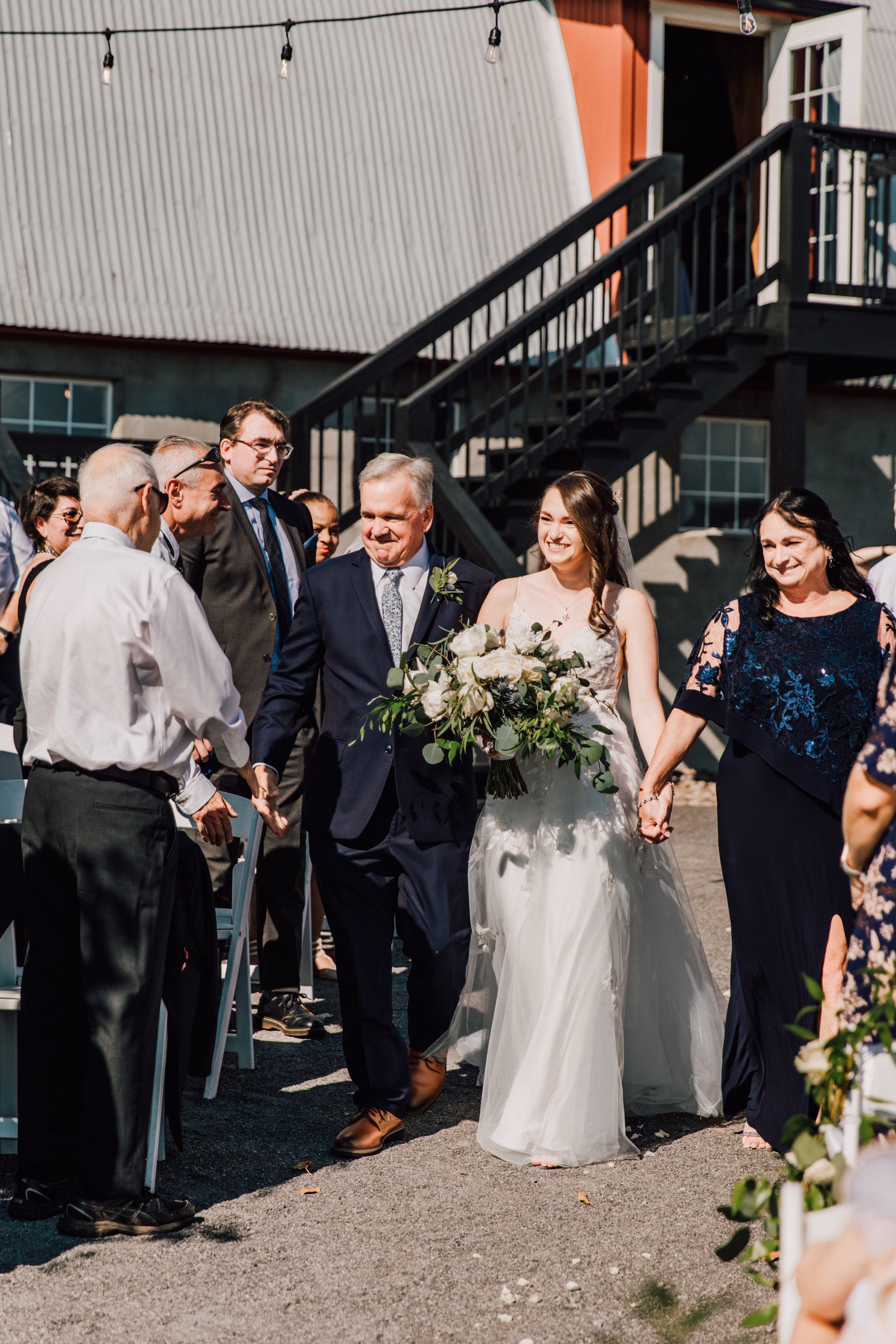  Bride walks down the aisle at outdoor wedding ceremony at Hayloft on the Arch 