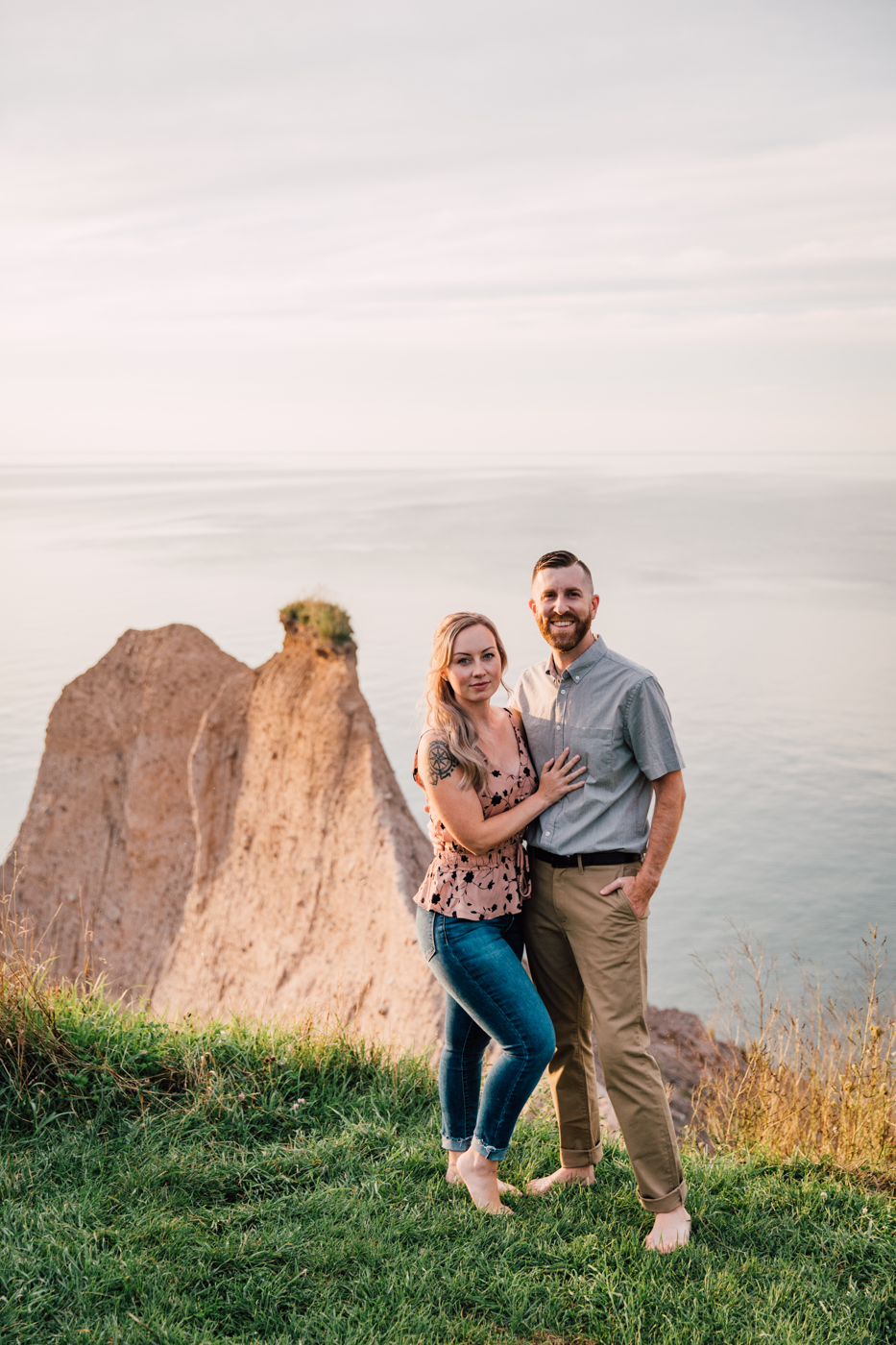  Engaged couple embraces while looking at the camera with the bluffs Oswego behind them 