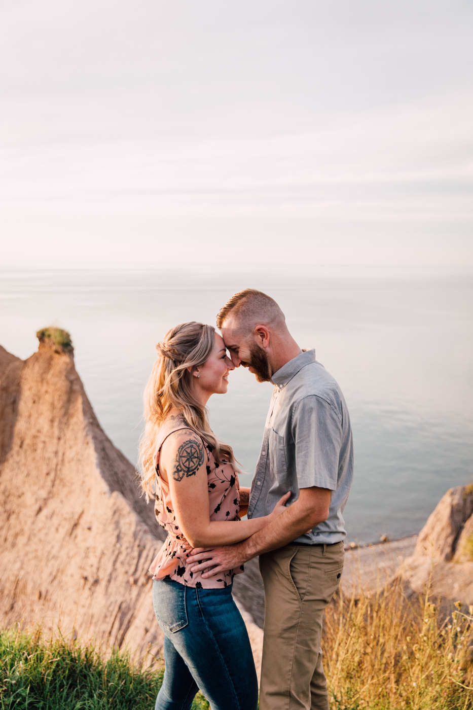  An engaged couple stands forehead to forehead during sunset engagement photos along Lake Ontario in Oswego NY 