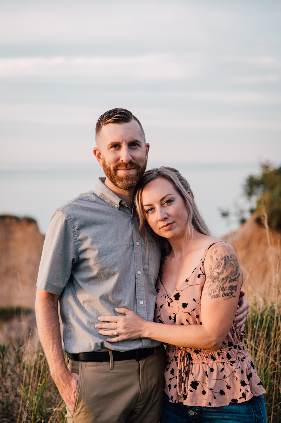  A couple stands along the shores of Lake Ontario posing for their sunset engagement photos with Brittany Juravich 