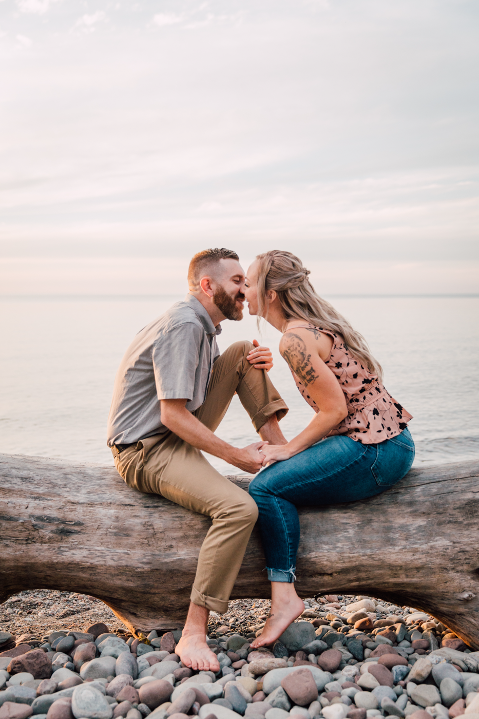  Engaged couple sits on an old log along the shores of Lake Ontario during sunset engagement photos 