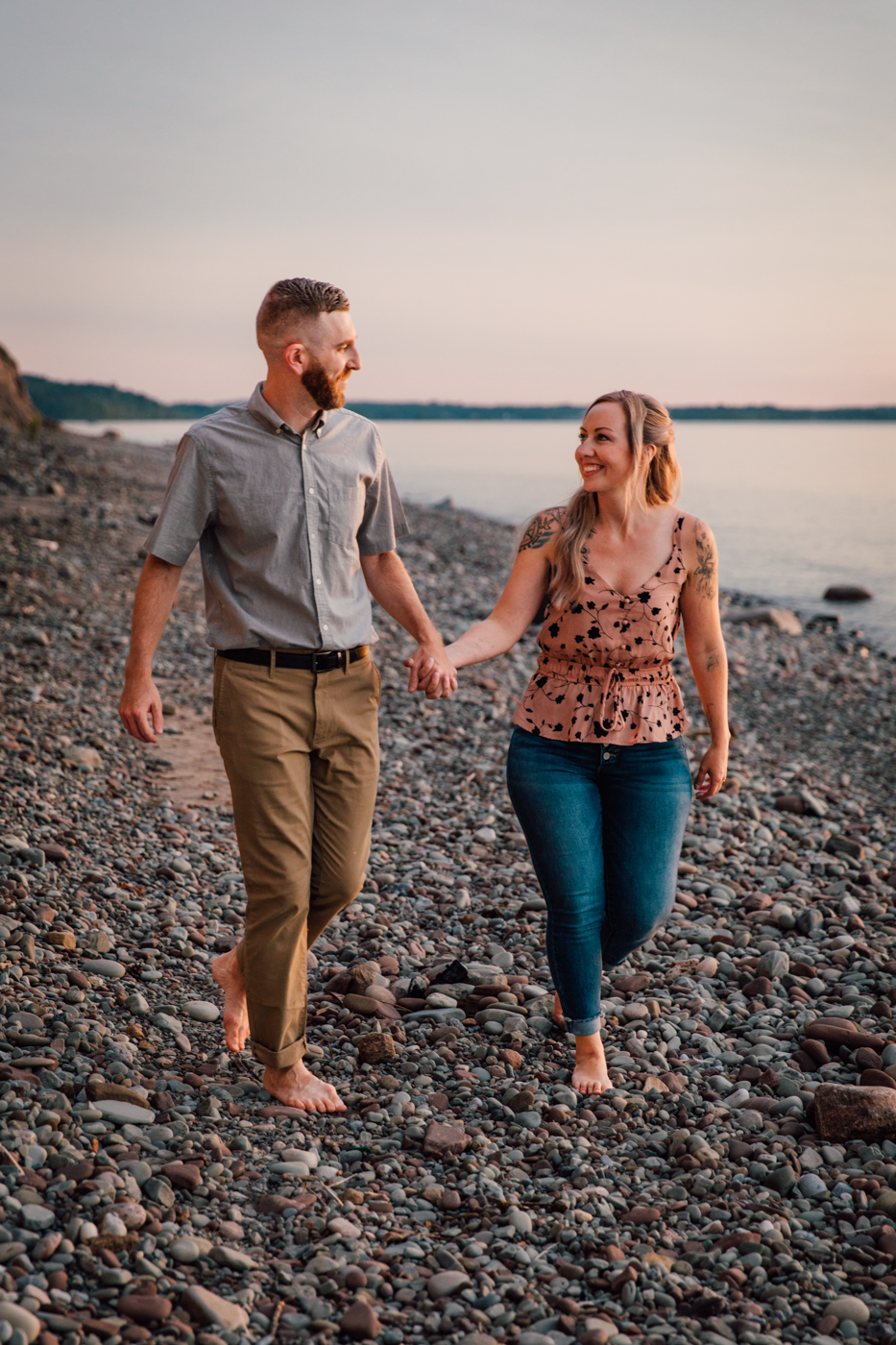 Engaged couple holds hands as they walk along the shores of Lake Ontario during engagement photography session with Brittany Juravich 