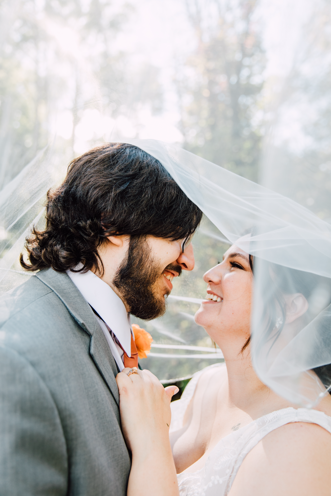  Bride and Groom smile at each other underneath the Bride’s veil leading up to their outdoor wedding ceremony at Sinclair of Skaneateles 